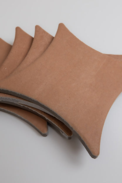 Four Finca Arcilla sample tiles, terracotta-colored and square with curved edges, stacked on a plain light surface.