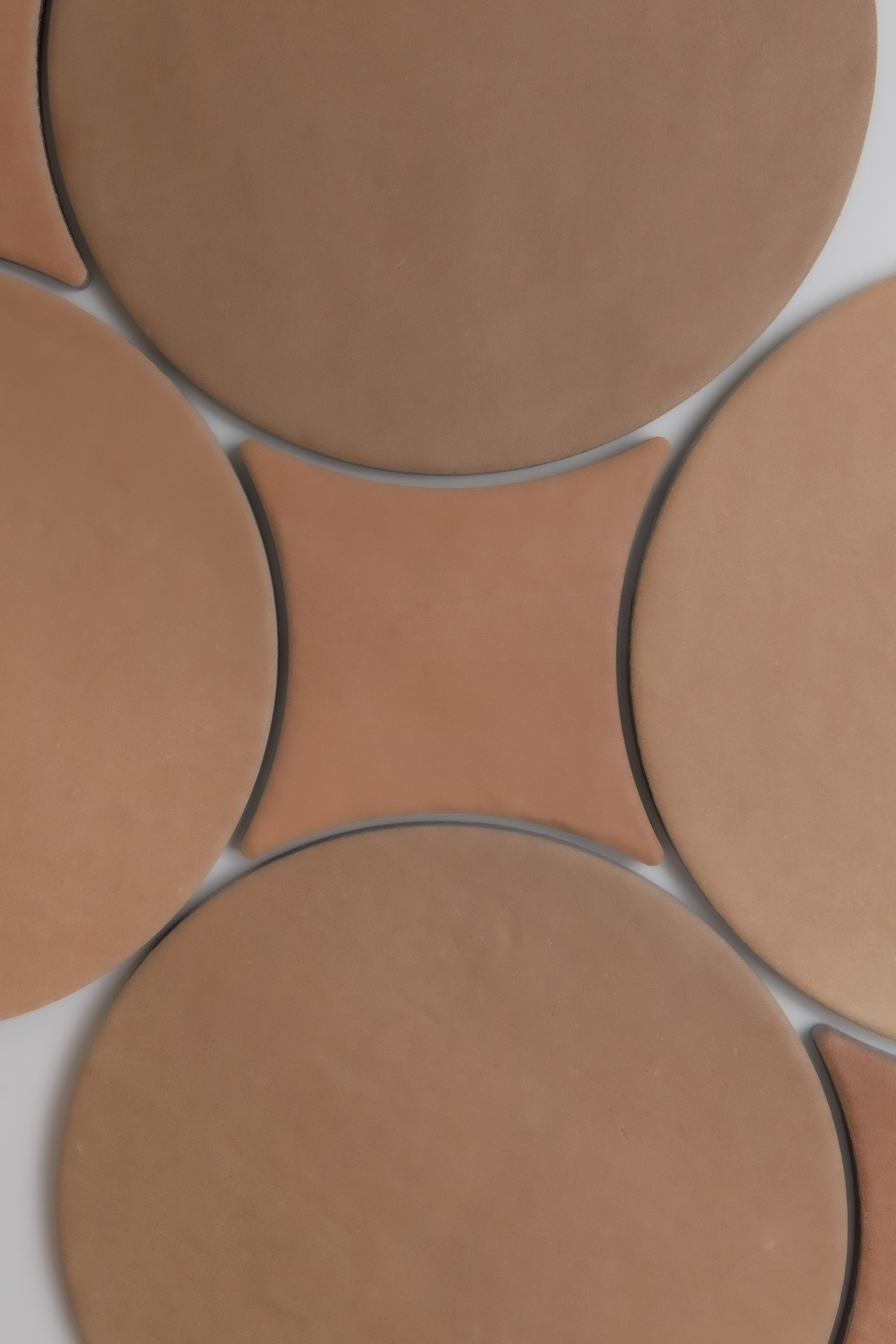 Arcilla sample tiles by Finca feature round and diamond tan shapes in a geometric pattern on a flat surface.