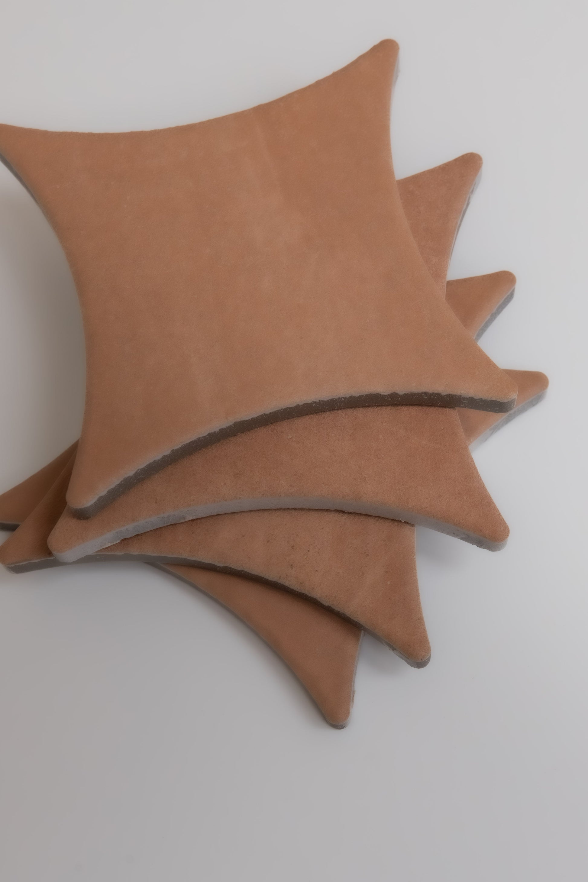 Four tan, star-shaped Arcilla ceramic tile samples by Finca stacked on a white surface, viewed from above.