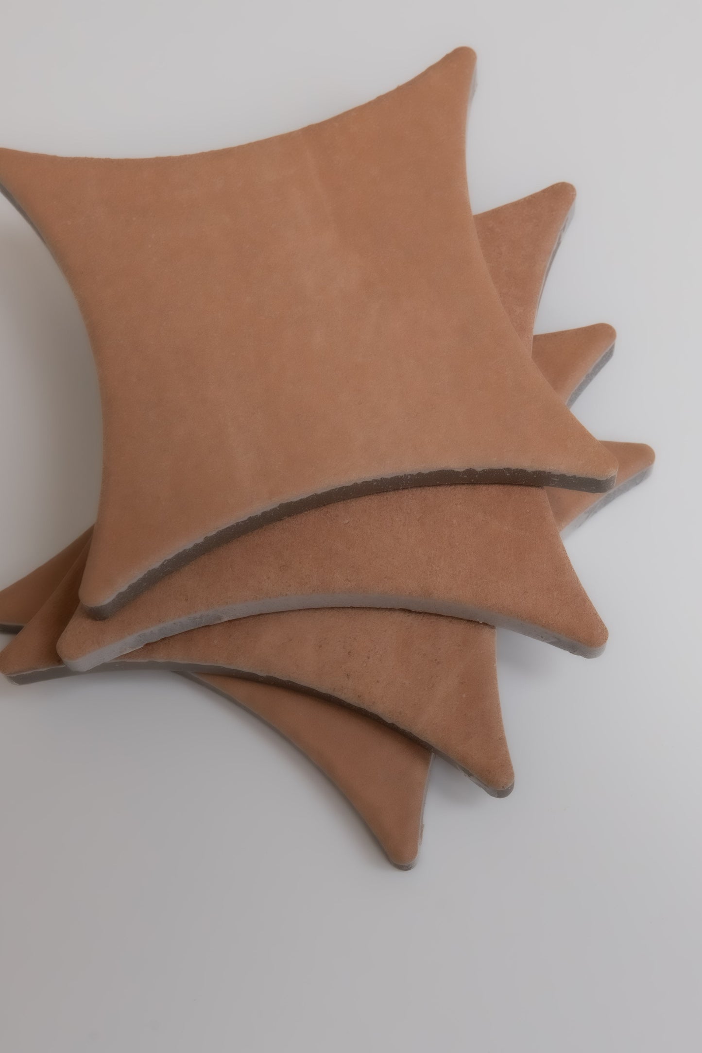 Four tan, star-shaped Arcilla ceramic tile samples by Finca stacked on a white surface, viewed from above.