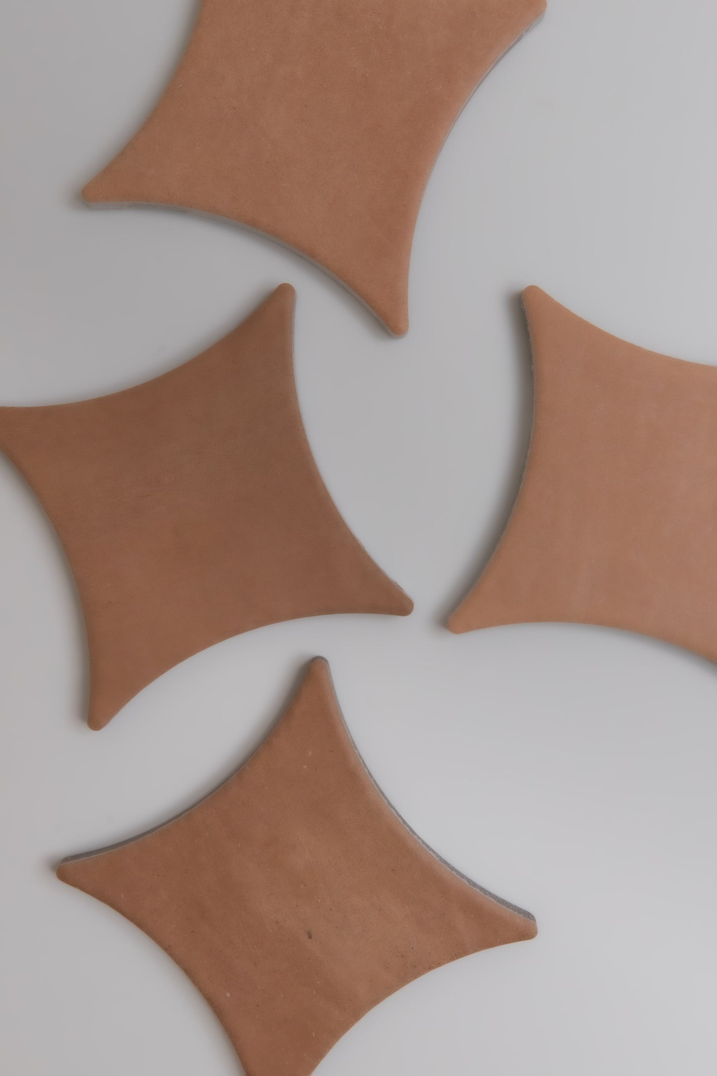 Four Arcilla sample tiles by Finca, brown and diamond-shaped with curved edges, are on a light gray background.