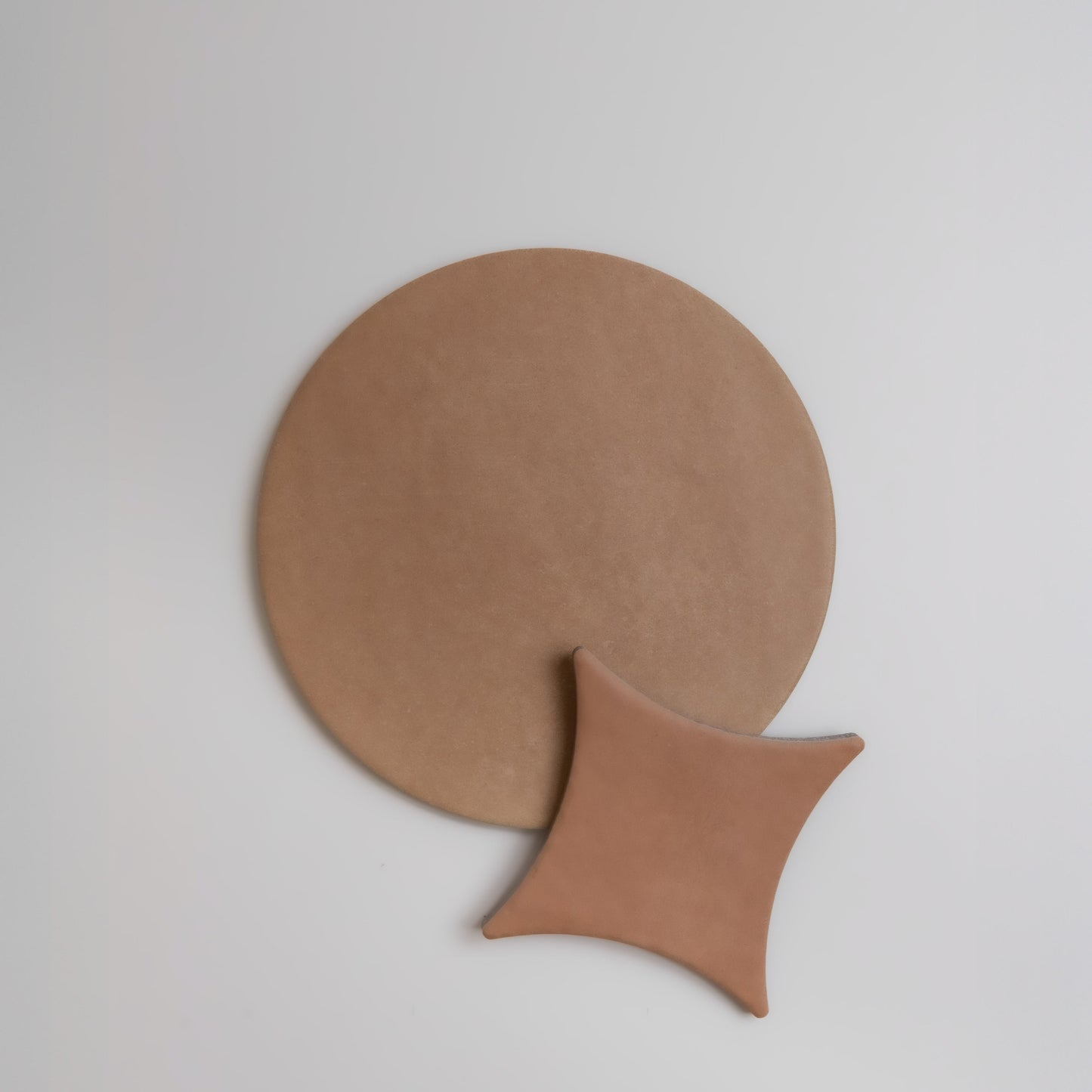 A round brown "Arcilla, Sample" mat and a brown cushion by Finca on a light gray background.