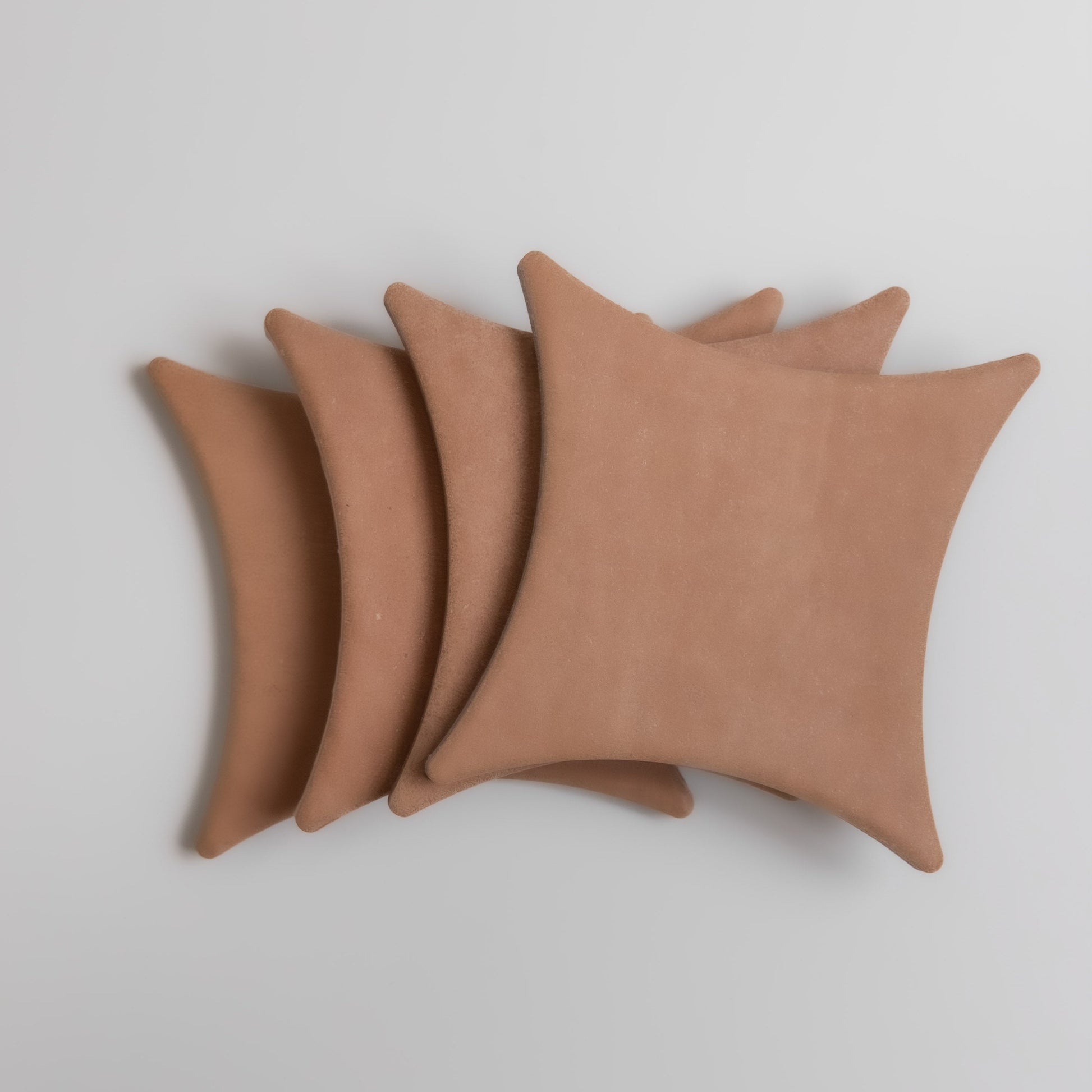 Four tan, square Arcilla cushions by Finca with pointed corners, stacked on a white background.