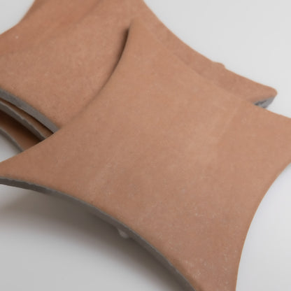 Three curved, terracotta-colored Arcilla samples by Finca overlap on a white background.