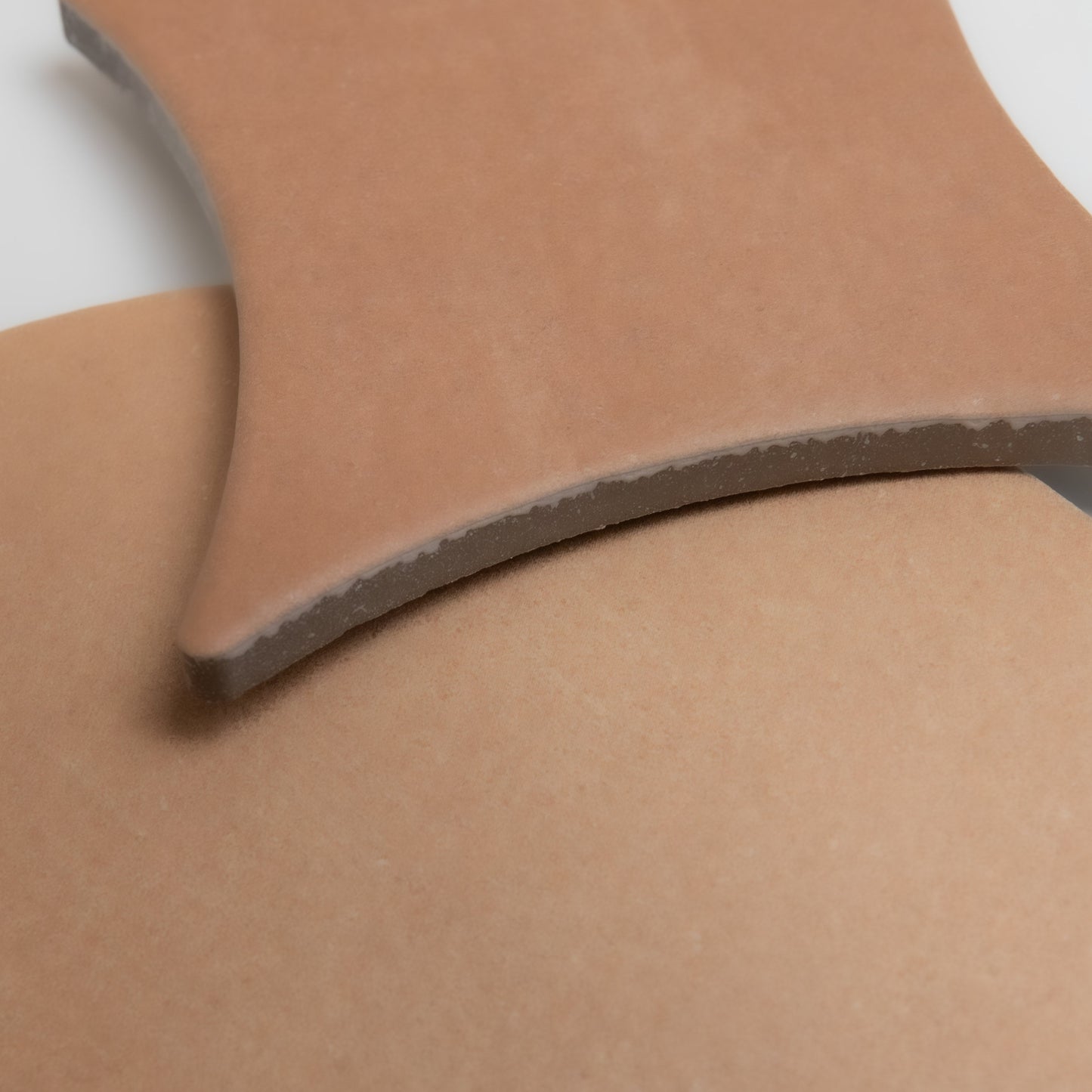 Close-up of two overlapping, curved pieces of Finca Arcilla Sample in matte light brown ceramic on a white surface.