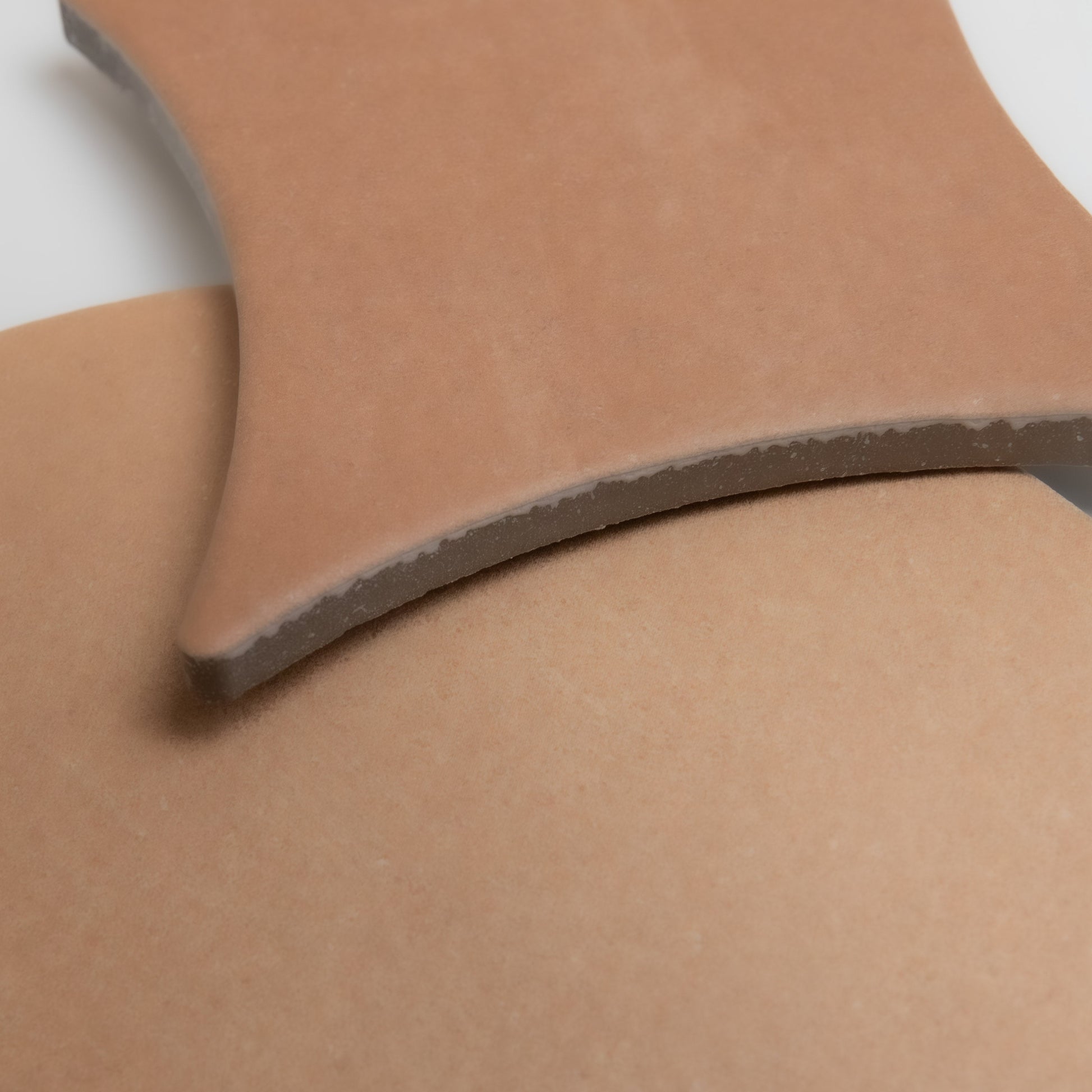 Close-up of two overlapping, curved pieces of Finca Arcilla Sample in matte light brown ceramic on a white surface.