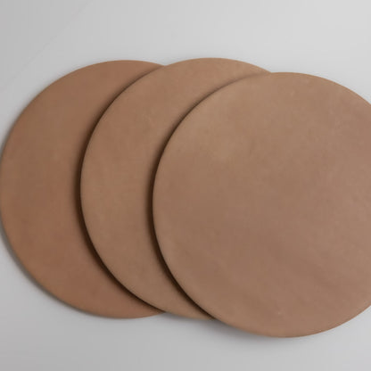 Three round, flat, brown Finca Arcilla samples overlap on a white surface.