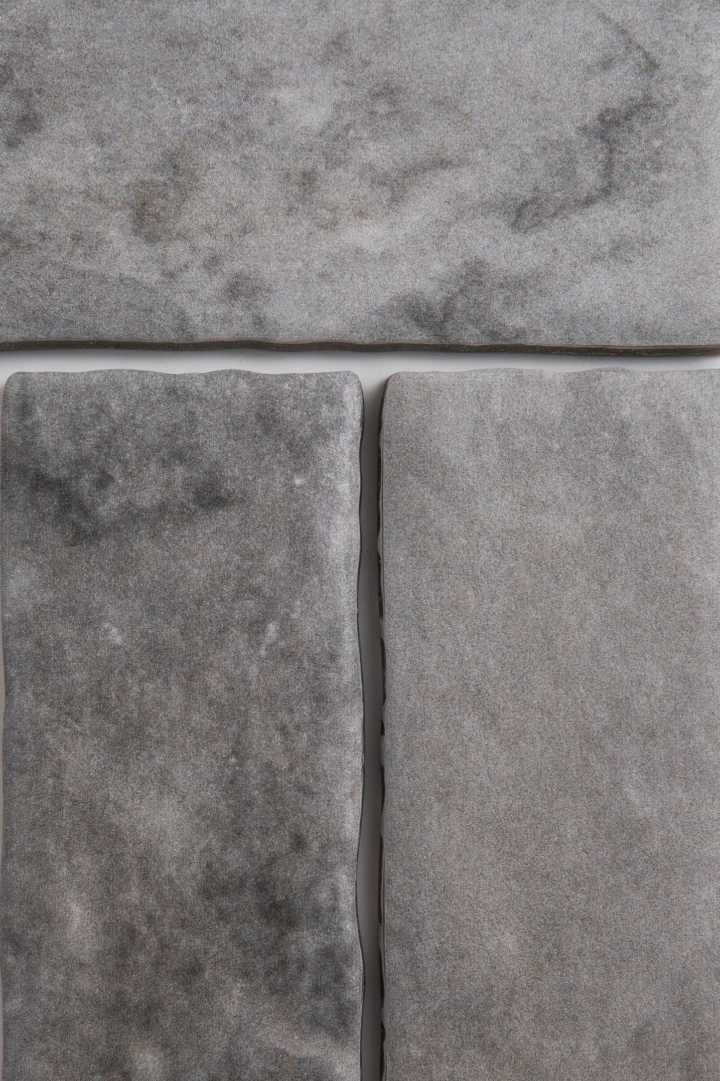 Close-up of three Bardiglio tiles by Tosca, gray with a marbled, slightly rough texture and visible grout lines.