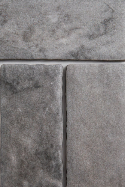 Close-up of three Bardiglio tiles by Tosca, gray with a marbled, slightly rough texture and visible grout lines.