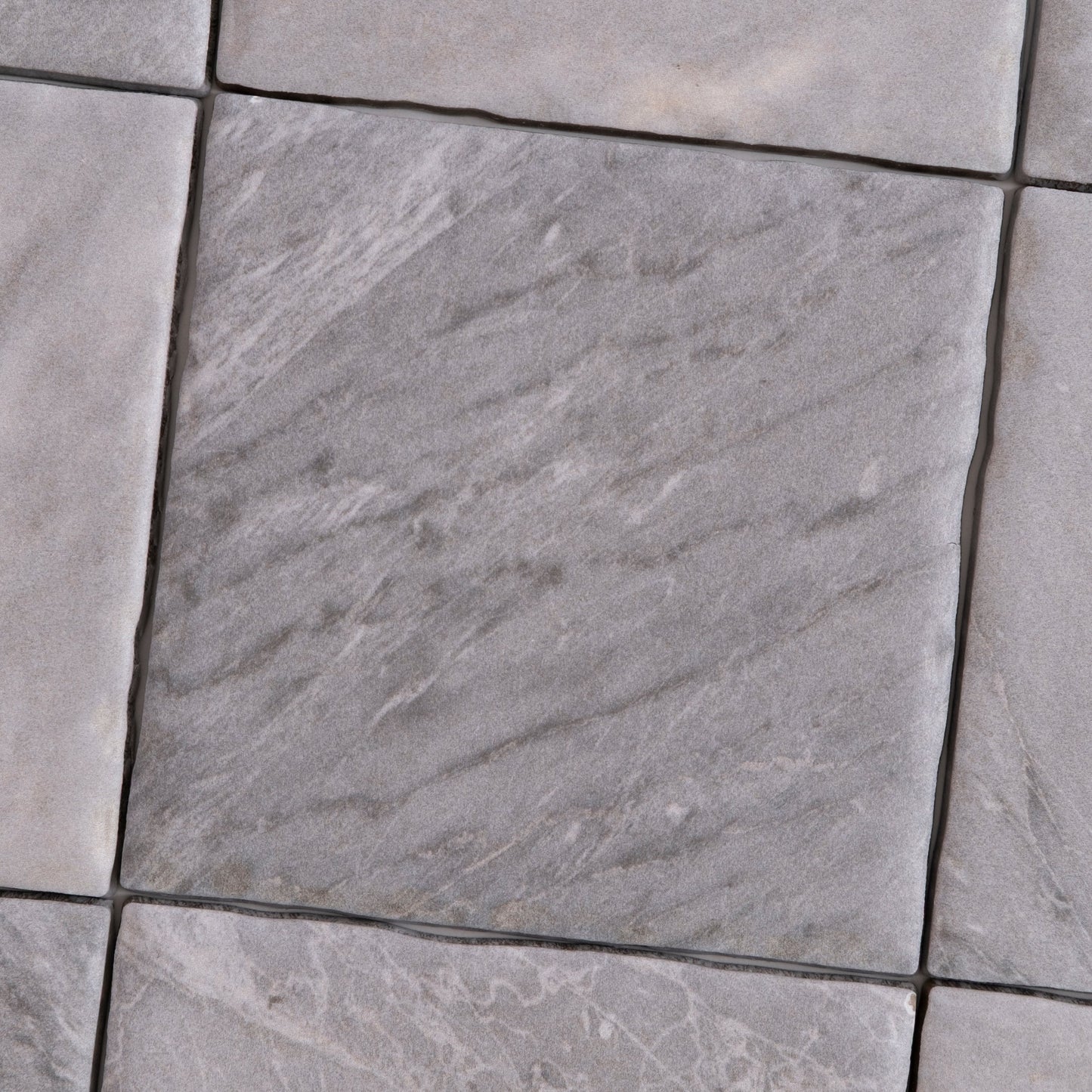 Close-up of Tosca Bardiglio sample: gray stone tiles with subtle texture and veining in a diagonal pattern.
