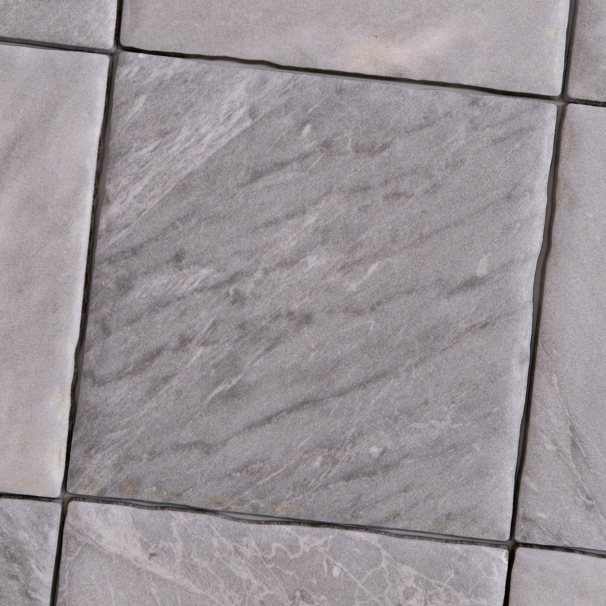 Close-up of Tosca Bardiglio sample: gray stone tiles with subtle texture and veining in a diagonal pattern.