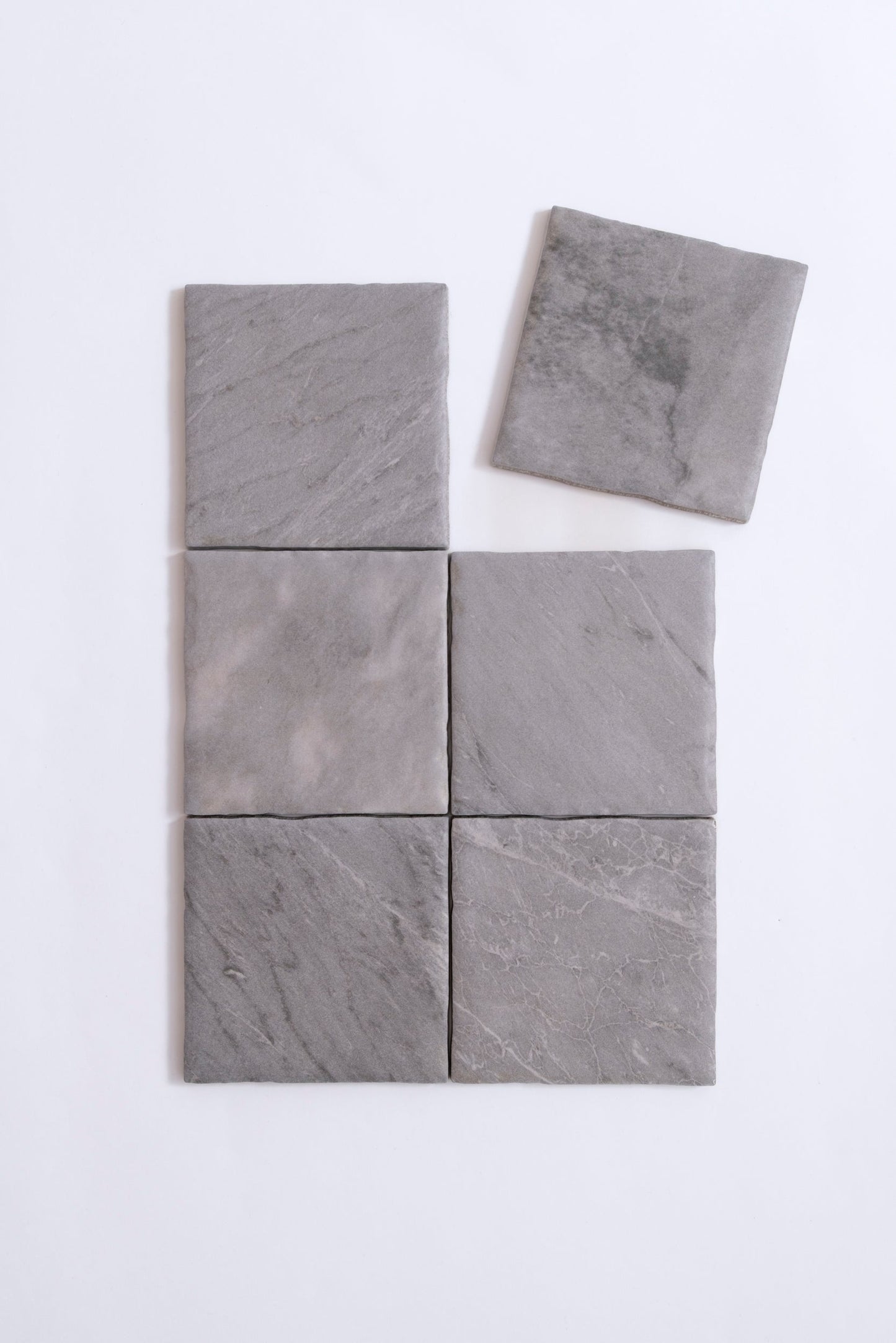Six Tosca Bardiglio tiles are arranged on a white surface, with one sample slightly separated at the top right.