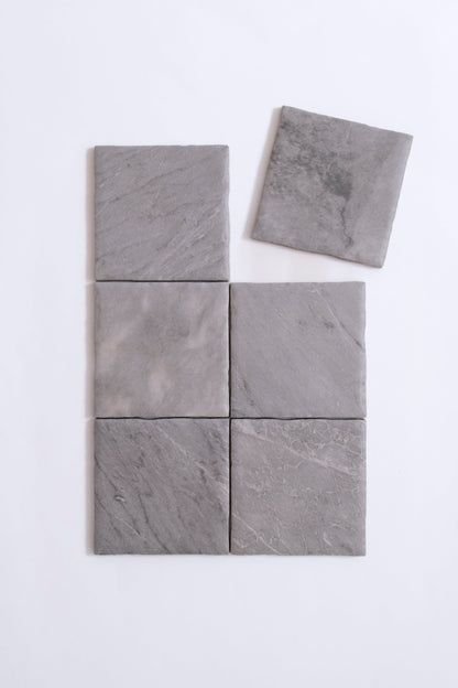 Six Tosca Bardiglio tiles are arranged on a white surface, with one sample slightly separated at the top right.