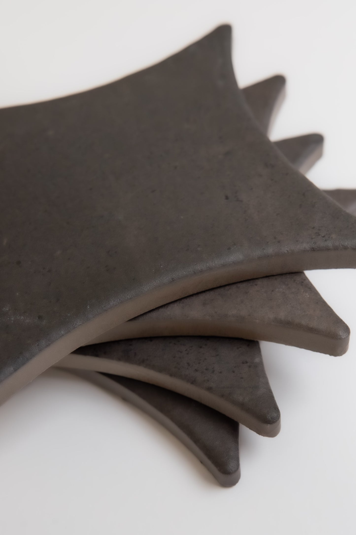 Four Finca Black Horse, Extra Sample ceramic coasters, dark and square with rounded edges, fanned on a white background.