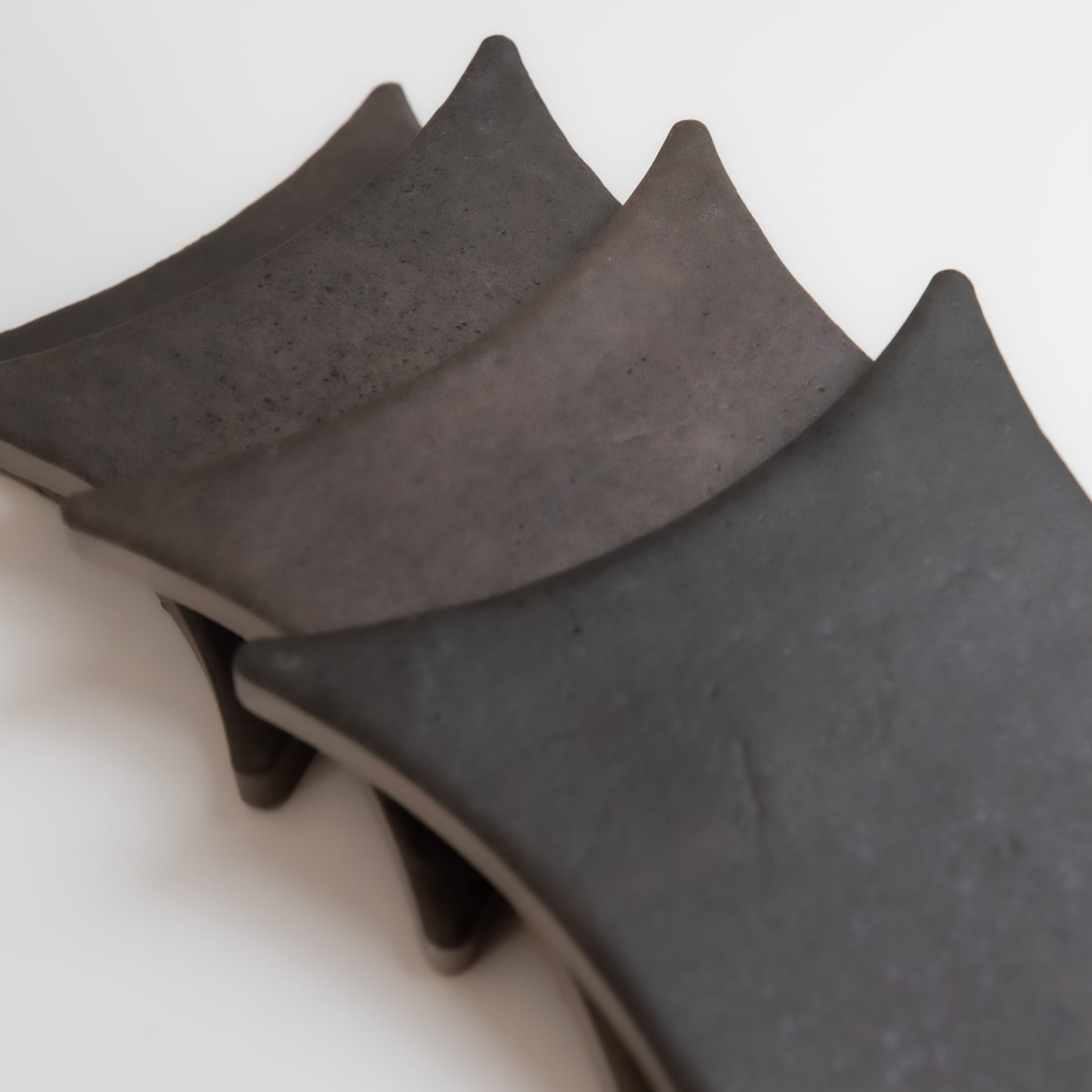 Three Black Horse, Extra Sample tiles by Finca, curved and stacked in layers, rest on a white surface.