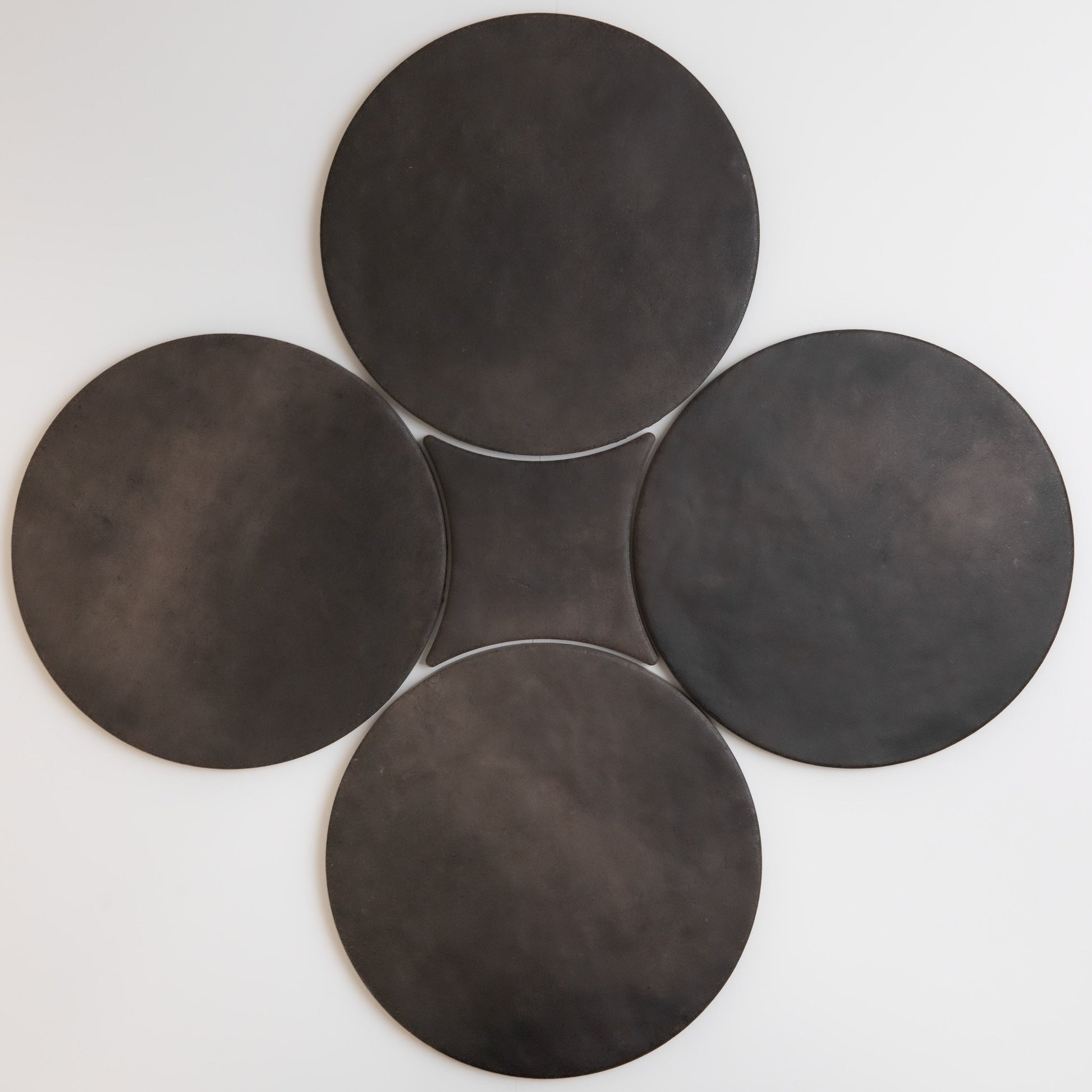 Four large, dark discs arranged in a clover shape on a light background by Finca, Black Horse Sample.