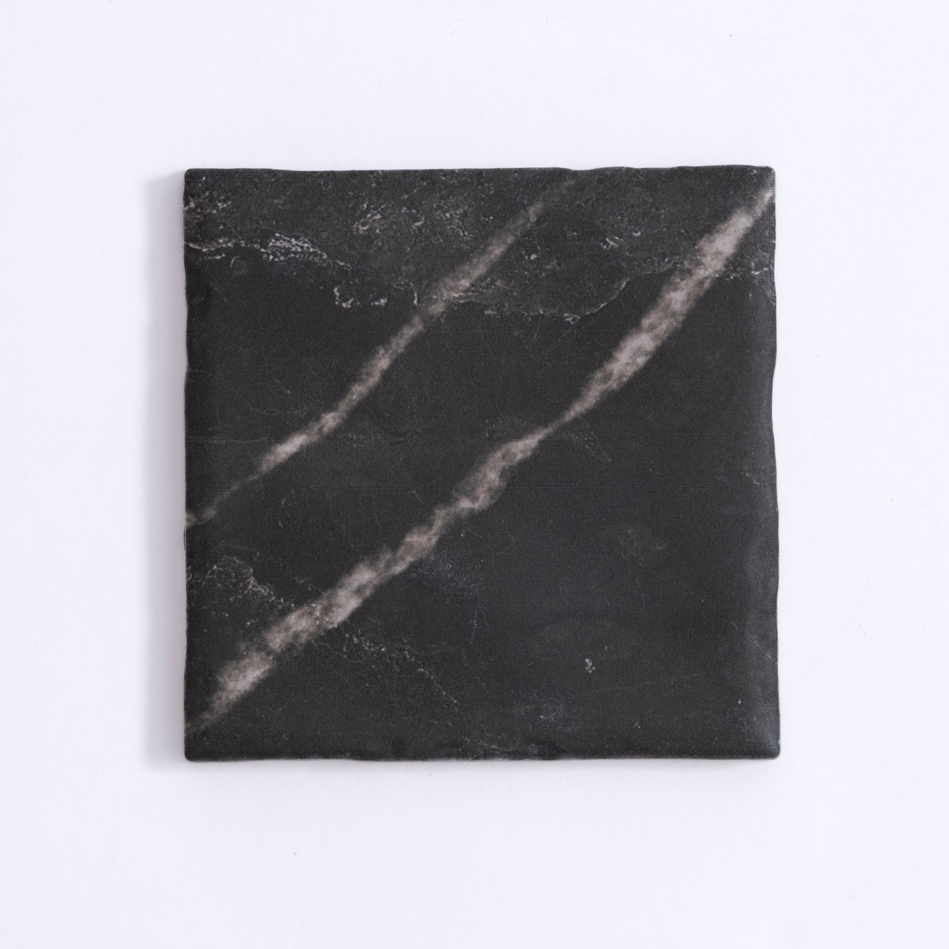The Tosca Black Marble, Extra Sample is a square black tile with faint white streaks and a slightly uneven surface.