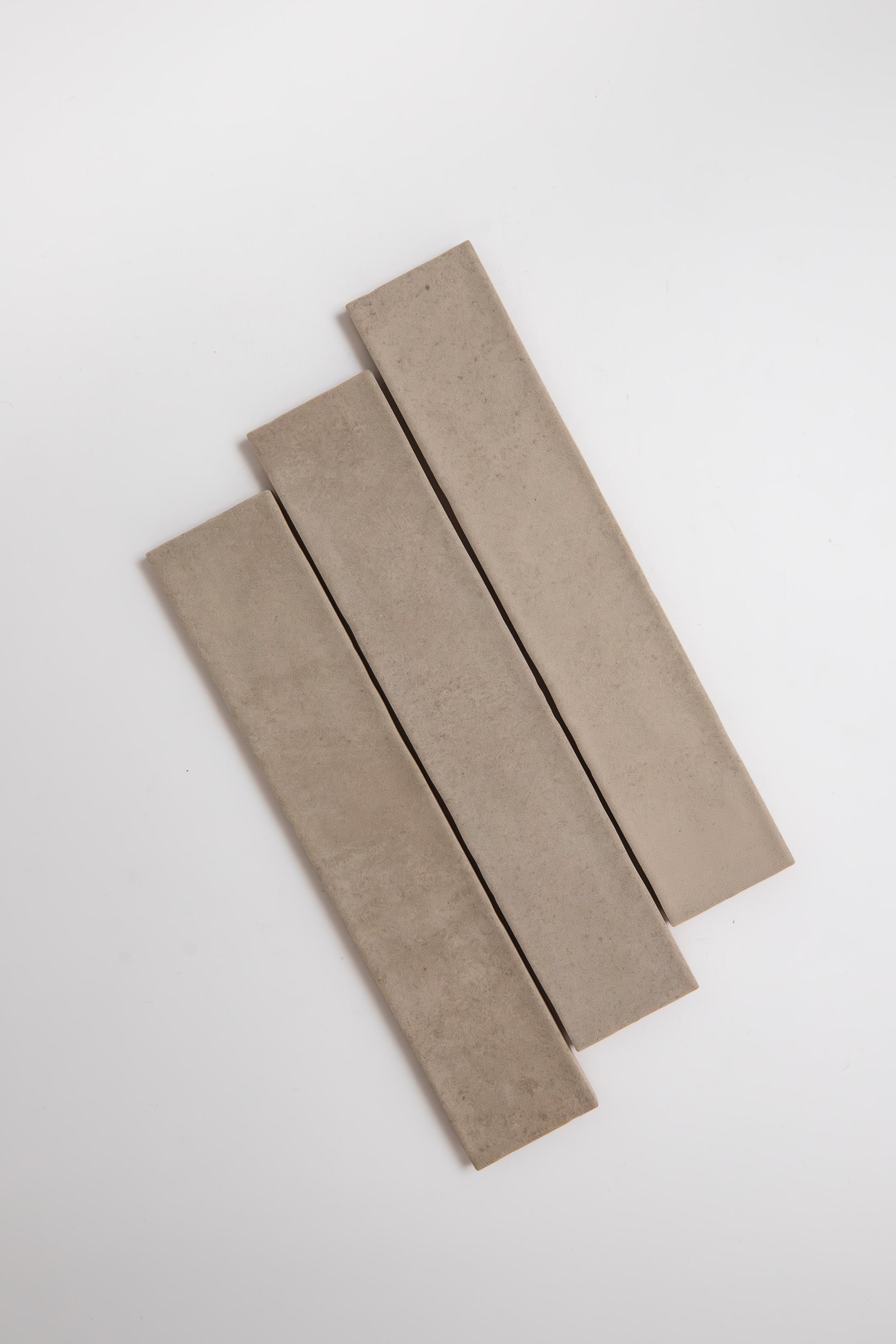 Three Buckland Beige tiles by Cottage Ivy are arranged diagonally and parallel on a white background.