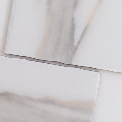 Two rectangular Tosca Calacatta Gold marble tiles with subtle gray and beige veining on a white background.