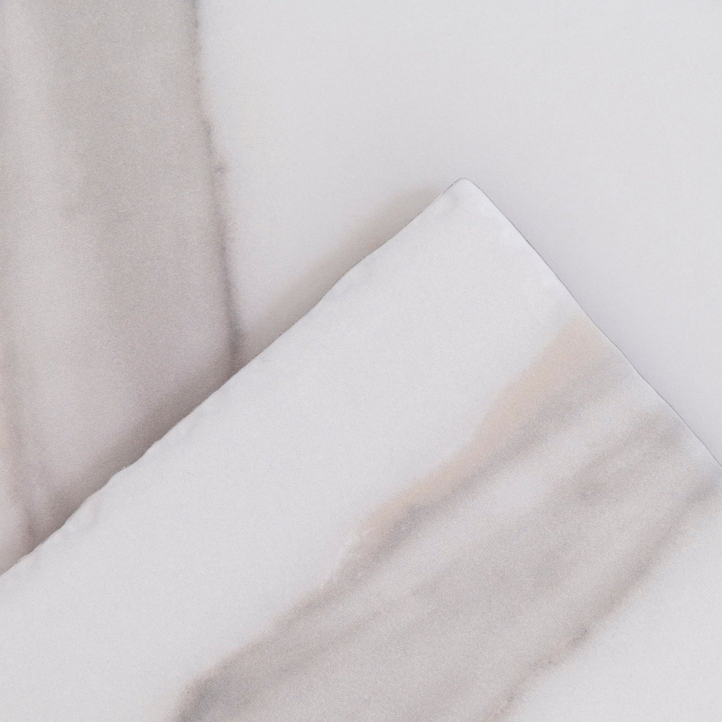 Two overlapping pieces of Tosca Calacatta Gold, light gray marble with soft wavy gray and beige veining.