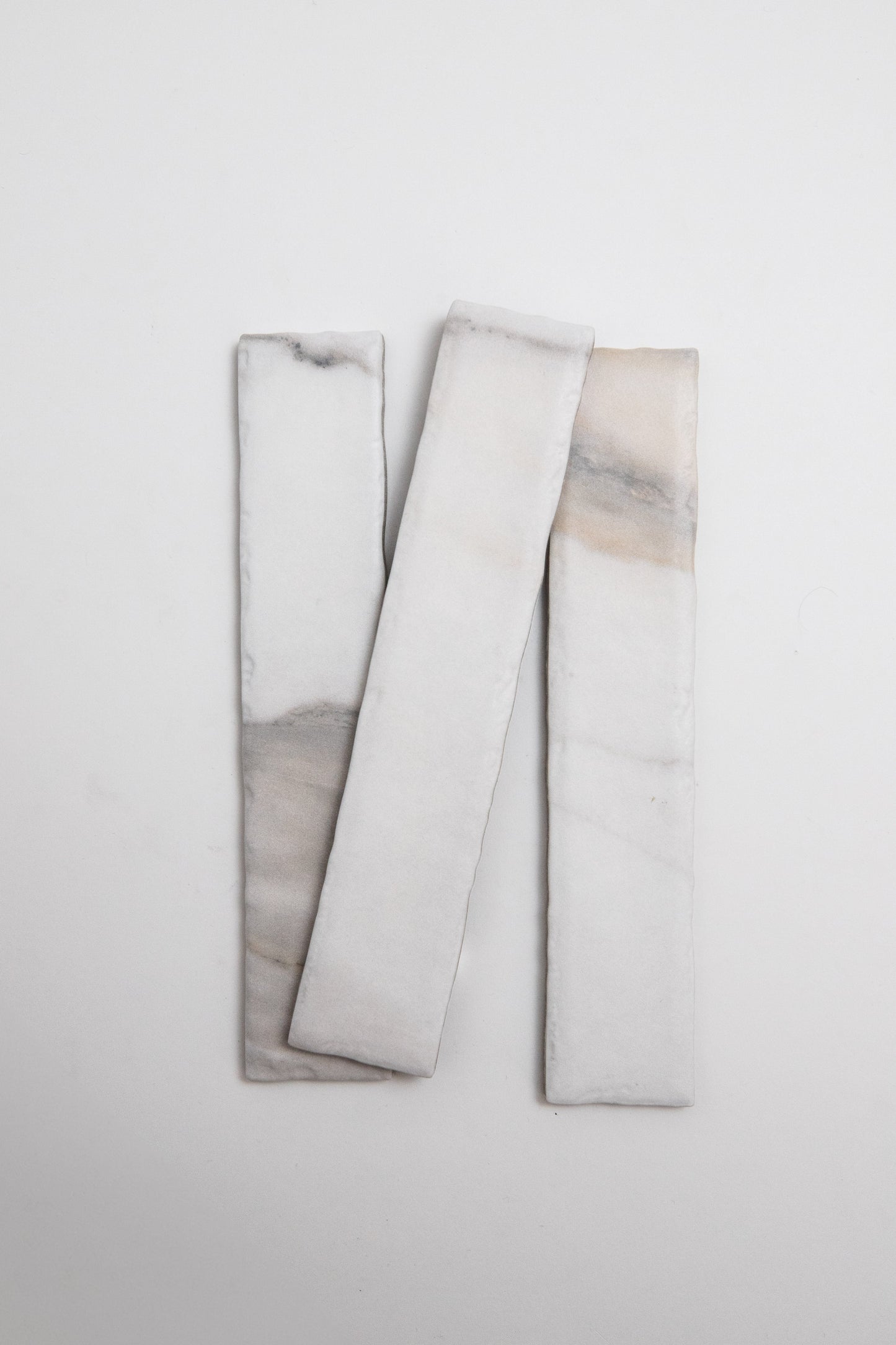 Three Tosca Calacatta Gold rectangular white tiles with soft gray and beige veining on a plain white background.