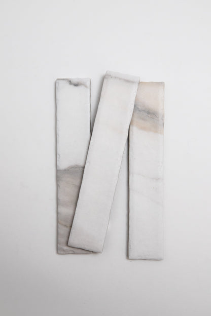 Three Tosca Calacatta Gold rectangular white tiles with soft gray and beige veining on a plain white background.