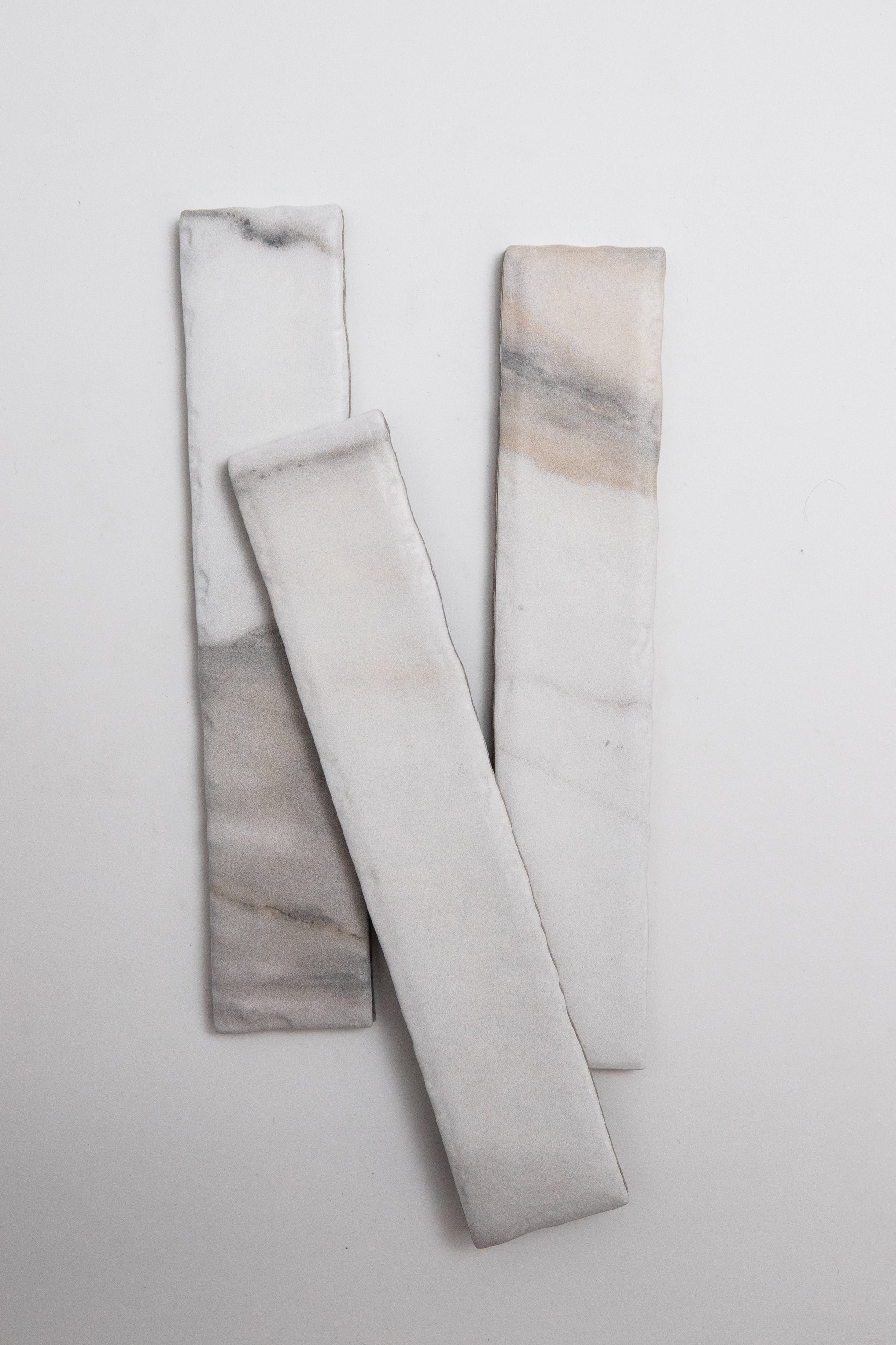 Three Tosca Calacatta Gold marble tiles with subtle gray and beige veining on a plain white background.