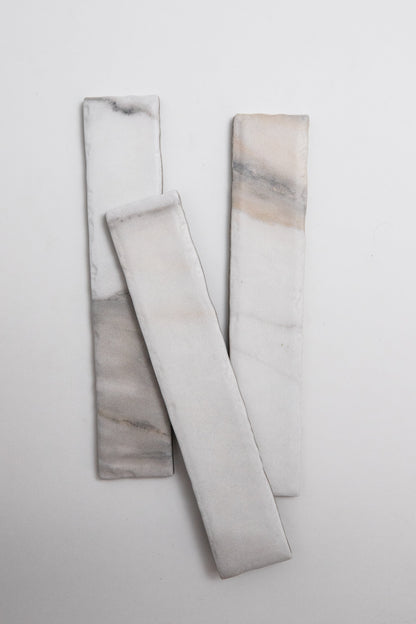 Three Tosca Calacatta Gold marble tiles with subtle gray and beige veining on a plain white background.