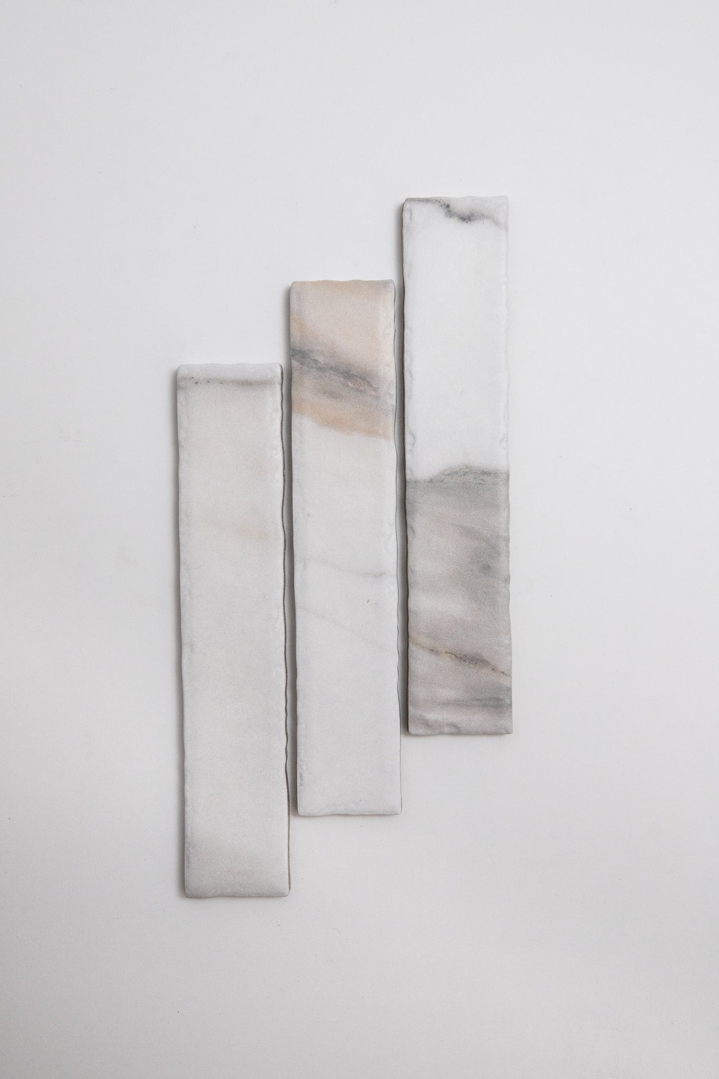 Three Tosca Calacatta Gold marble tiles with gray and beige veining arranged vertically on a white background.