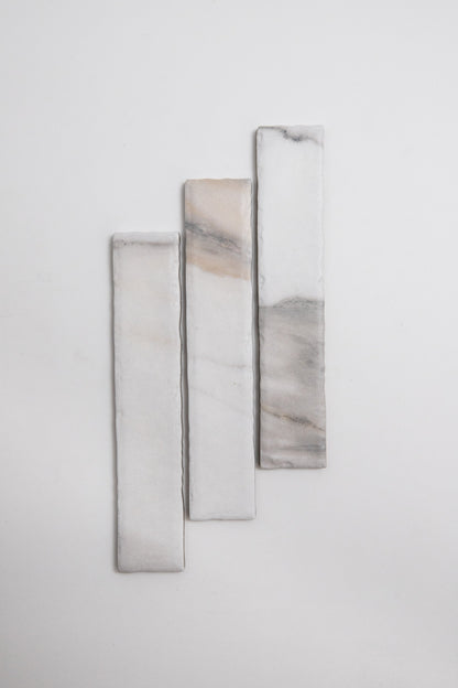 Three Tosca Calacatta Gold marble tiles with gray and beige veining arranged vertically on a white background.