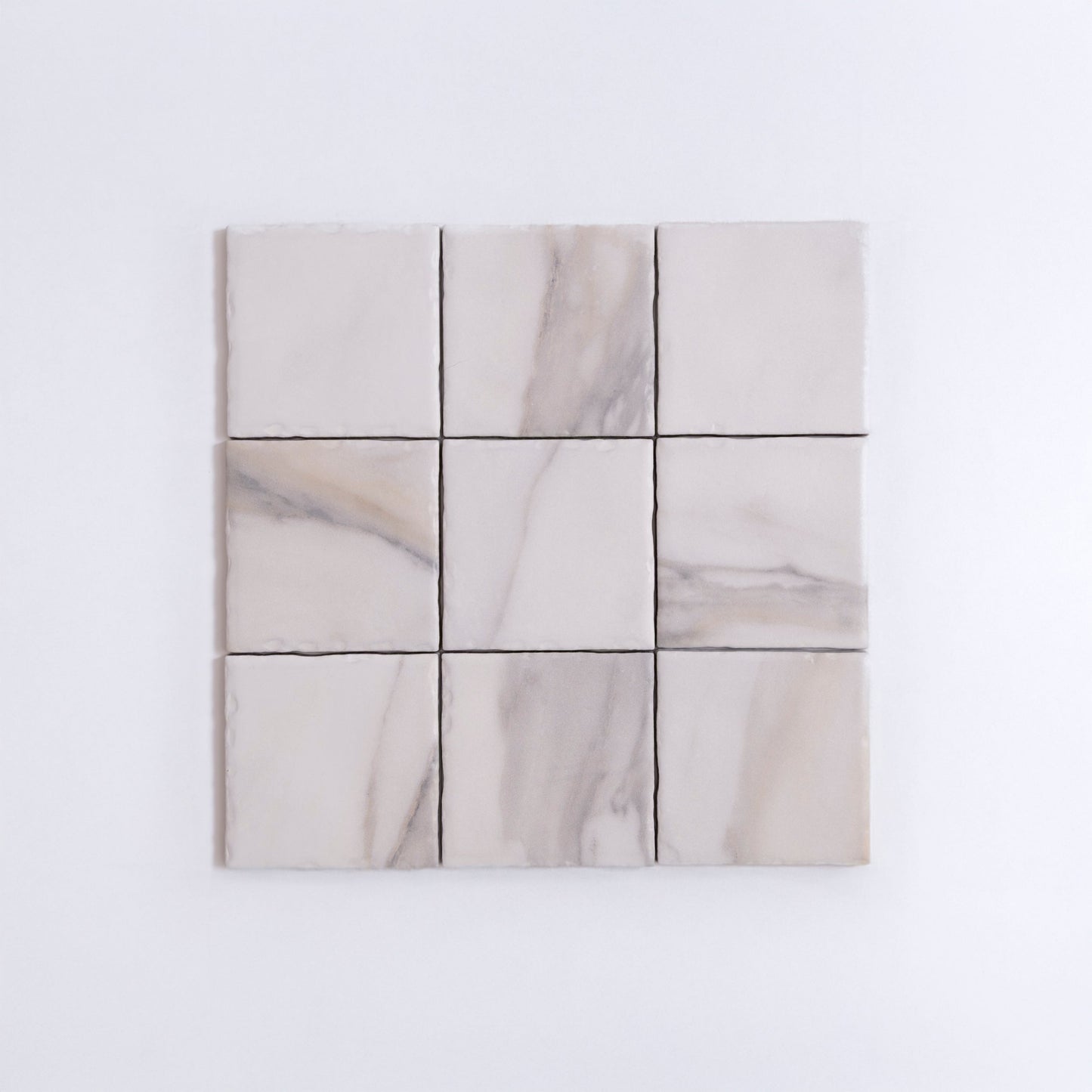Nine Calacatta Gold marble tiles by Tosca arranged in a grid, featuring subtle gray veining on a white background.