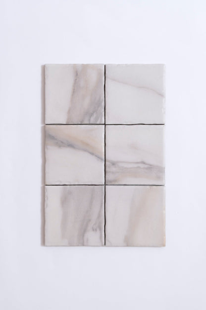 Six Tosca Calacatta Gold marble tiles with light gray and beige veining arranged in two rows on a white background.