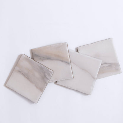 Four Tosca Calacatta Gold marble tiles with light gray and beige veining are arranged on a white background.