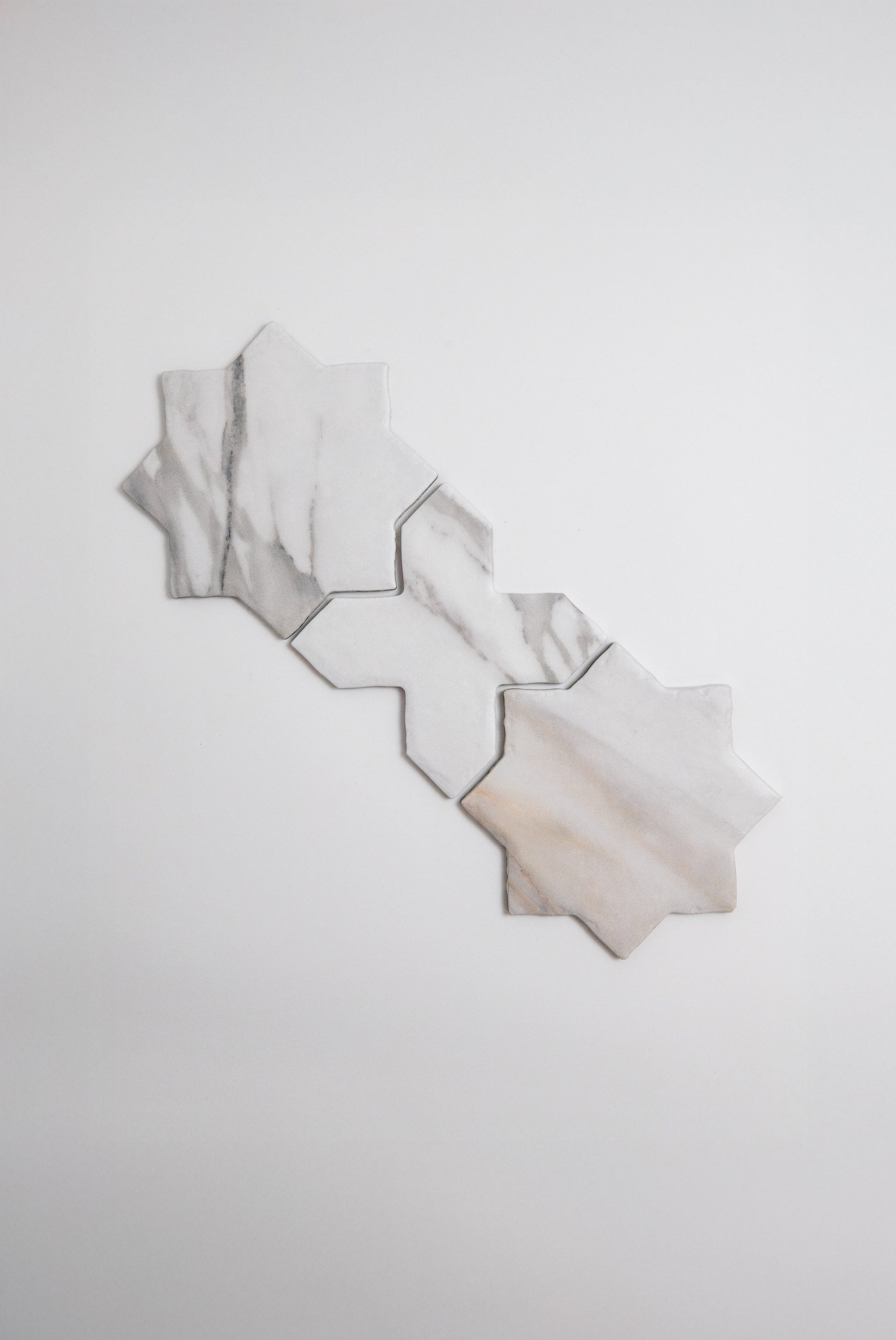 Four Tosca Calacatta Gold, Extra Sample marble tiles are arranged in a star shape on a white background.