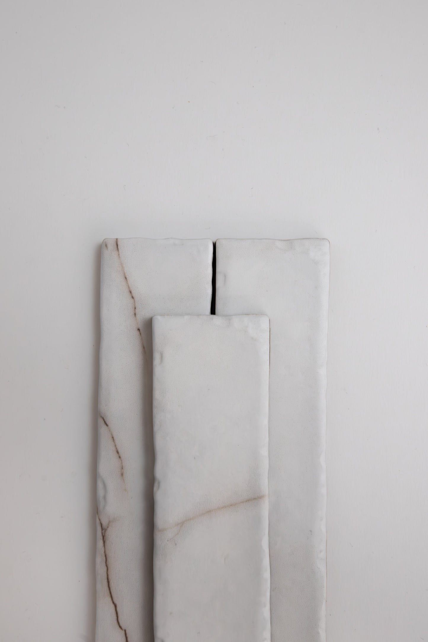 Three rectangular Calacatta Soft samples by Tosca, white with subtle brown lines, are stacked on a plain light background.