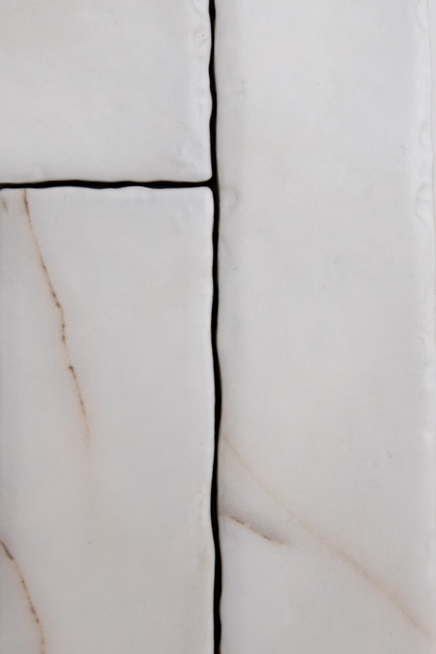 Close-up of four Tosca Calacatta Soft ceramic tiles with irregular edges and beige veining, separated by dark grout.