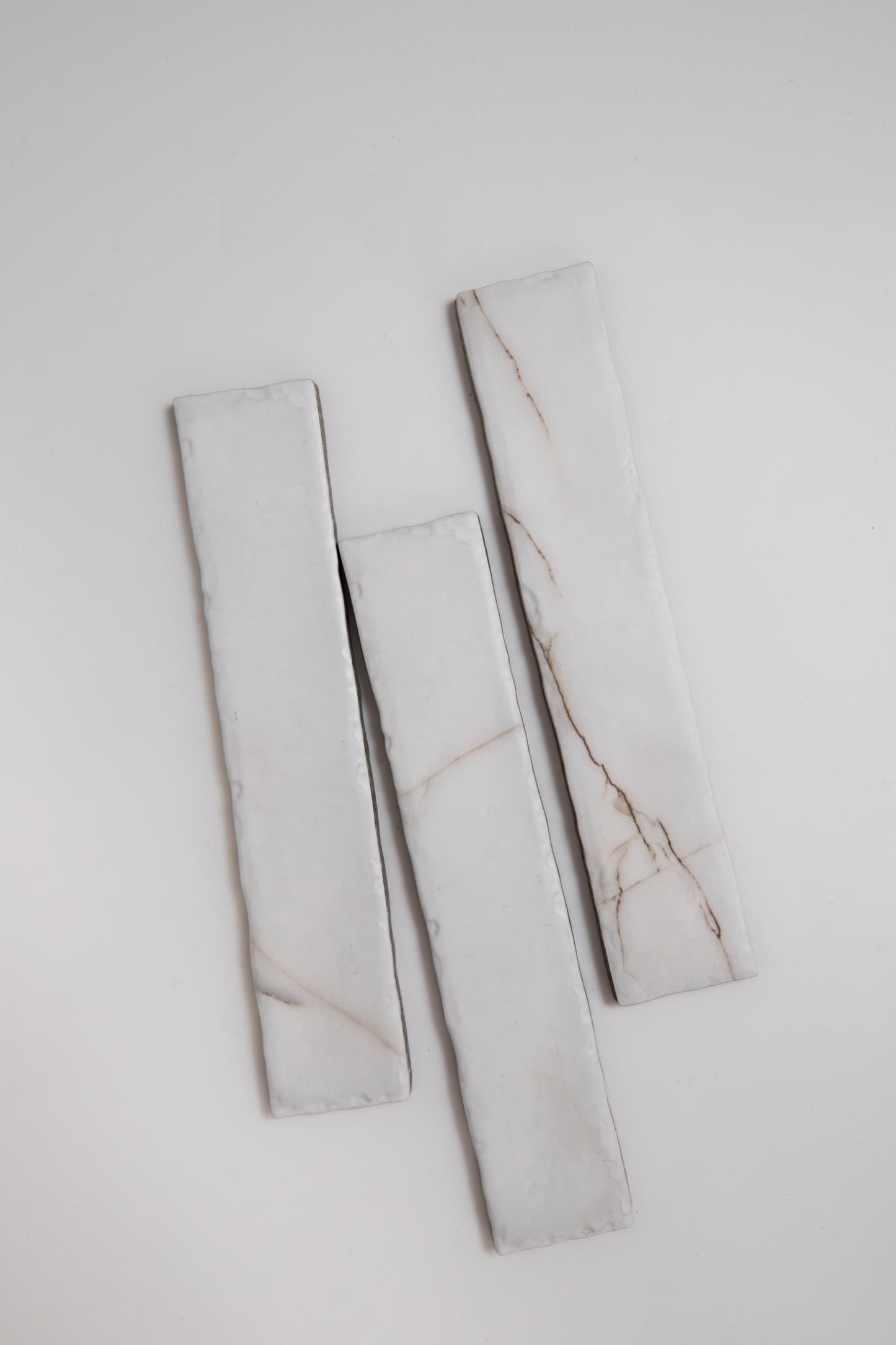 Three Tosca Calacatta Soft rectangular white marble sample tiles with thin brown veins, arranged vertically on white.
