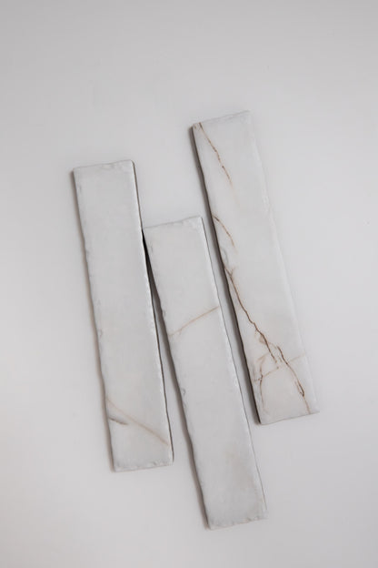 Three Tosca Calacatta Soft rectangular white marble sample tiles with thin brown veins, arranged vertically on white.