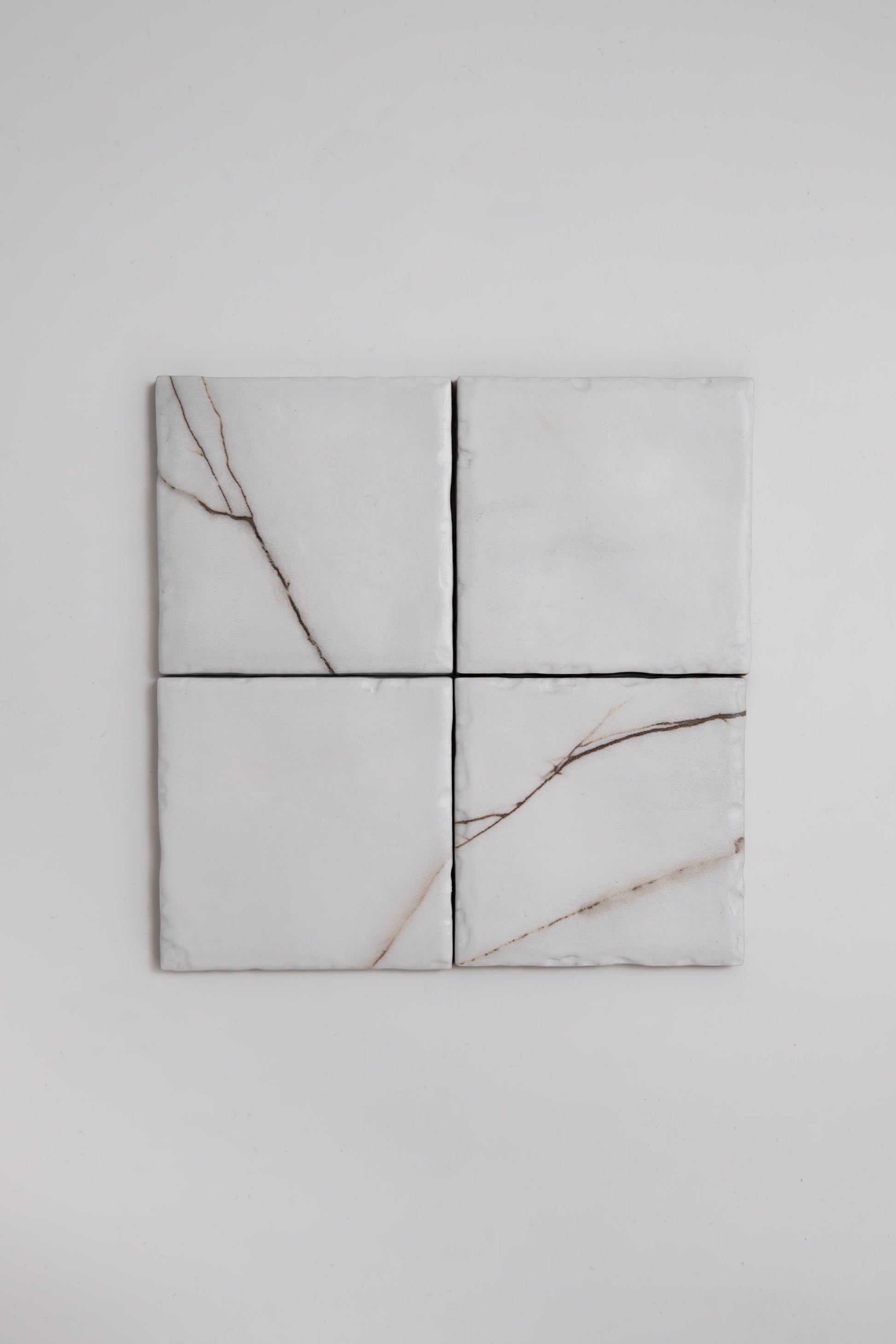 Four Tosca Calacatta Soft sample tiles with light brown veining are arranged in a 2x2 grid on a white wall.