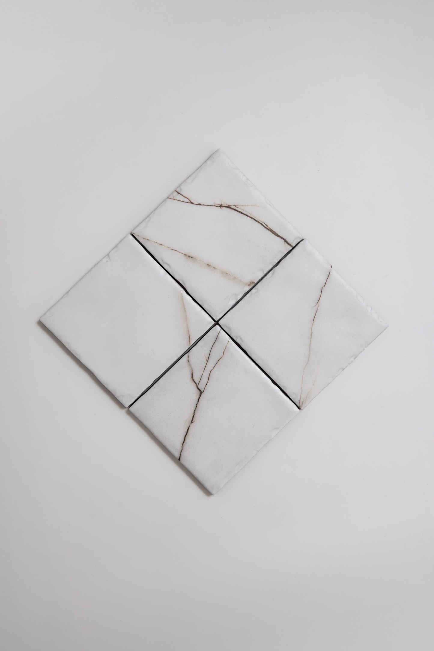 Four Calacatta Soft marble tile samples by Tosca with light brown veins are arranged in a diamond on a white background.