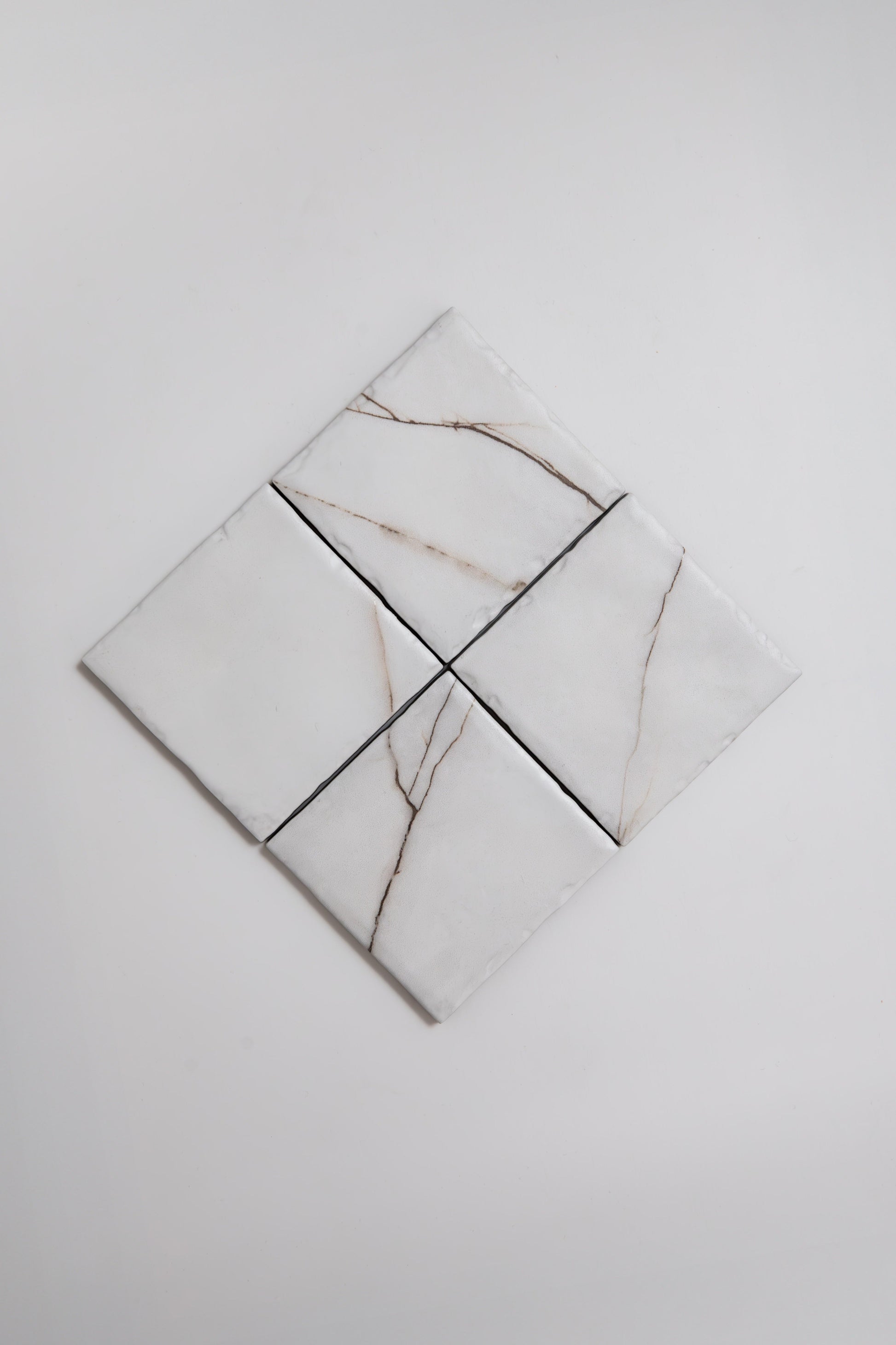 Four Calacatta Soft marble tile samples by Tosca with light brown veins are arranged in a diamond on a white background.