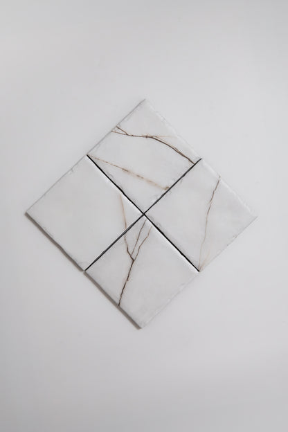 Four Calacatta Soft marble tile samples by Tosca with light brown veins are arranged in a diamond on a white background.
