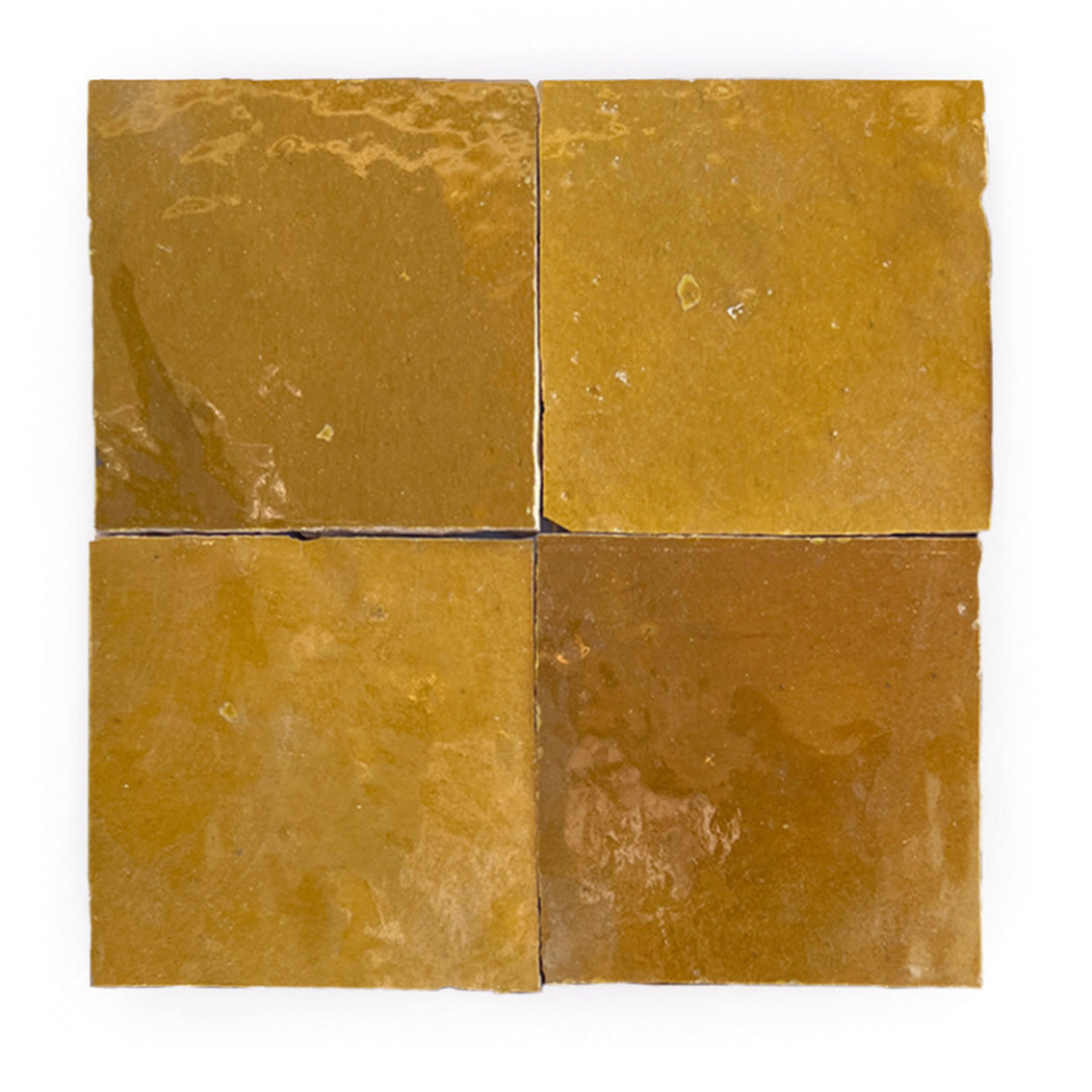 Four glossy, square mustard-yellow tiles arranged in a grid with slight color variations and subtle surface reflections.