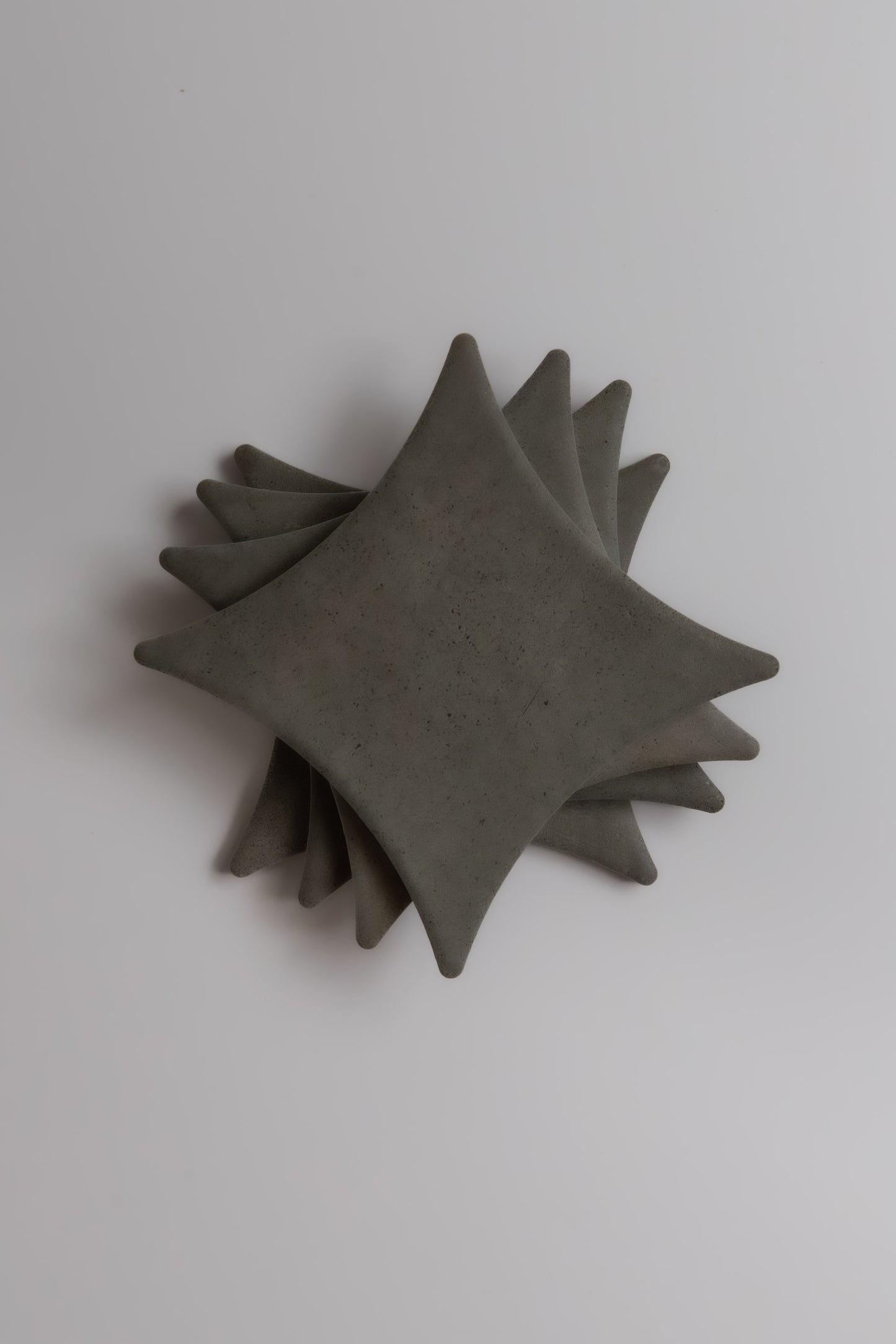 Stack of four square, gray Finca Cardon Extra Sample ceramic plates with pointed corners on a white background.