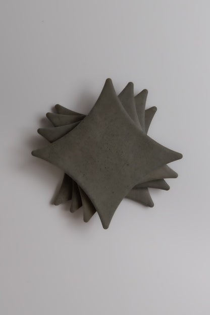 Stack of four square, gray Finca Cardon Extra Sample ceramic plates with pointed corners on a white background.
