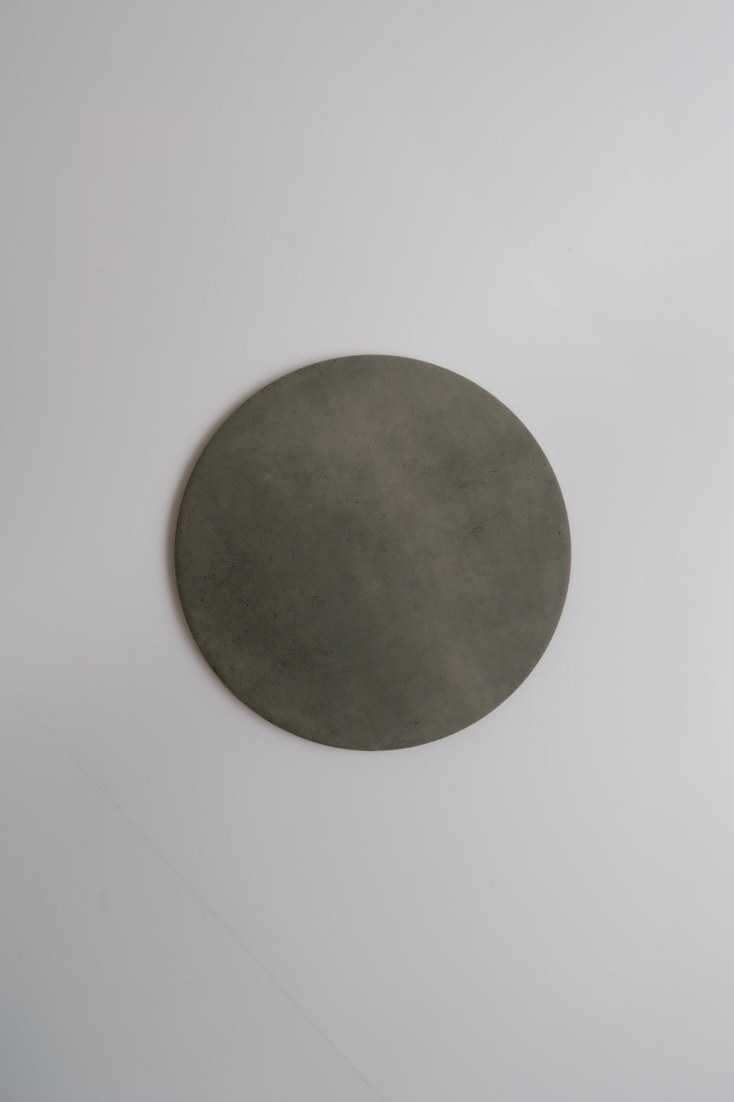A round, flat, gray Cardon, Sample stone by Finca placed on a plain white background.