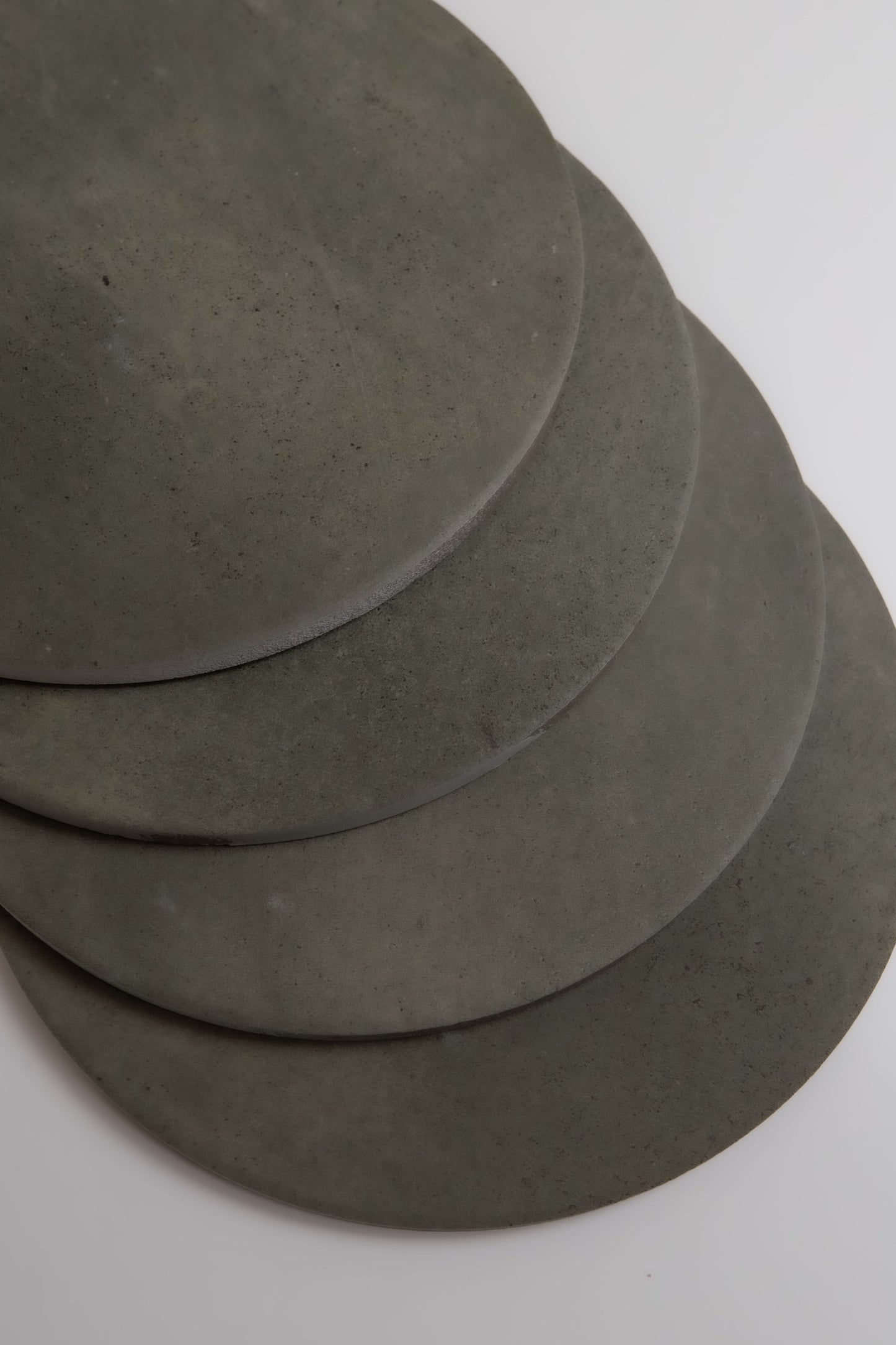 Four overlapping round gray Cardon stone slabs by Finca, arranged on a white surface.
