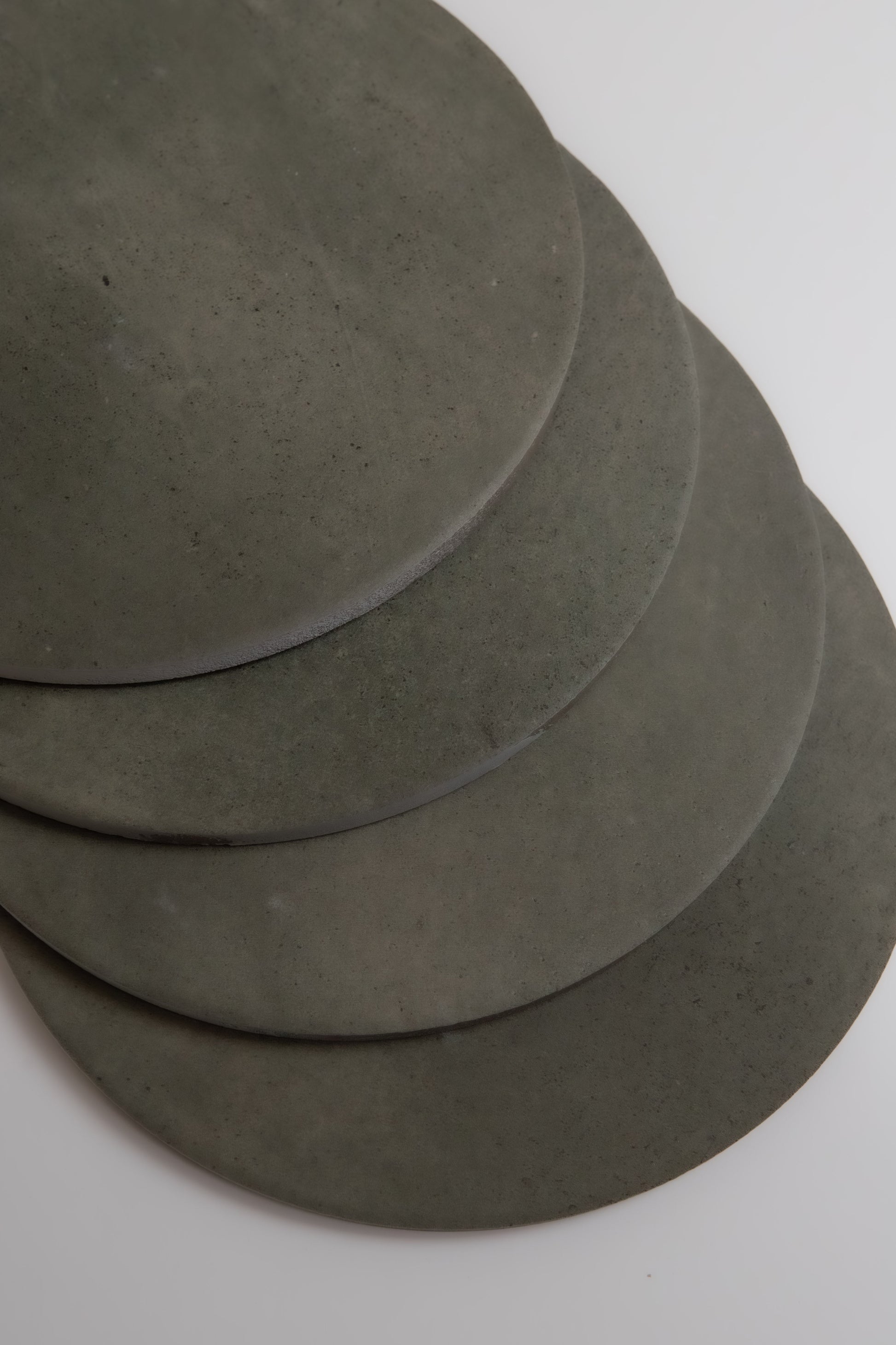 Four overlapping round gray Cardon stone slabs by Finca, arranged on a white surface.