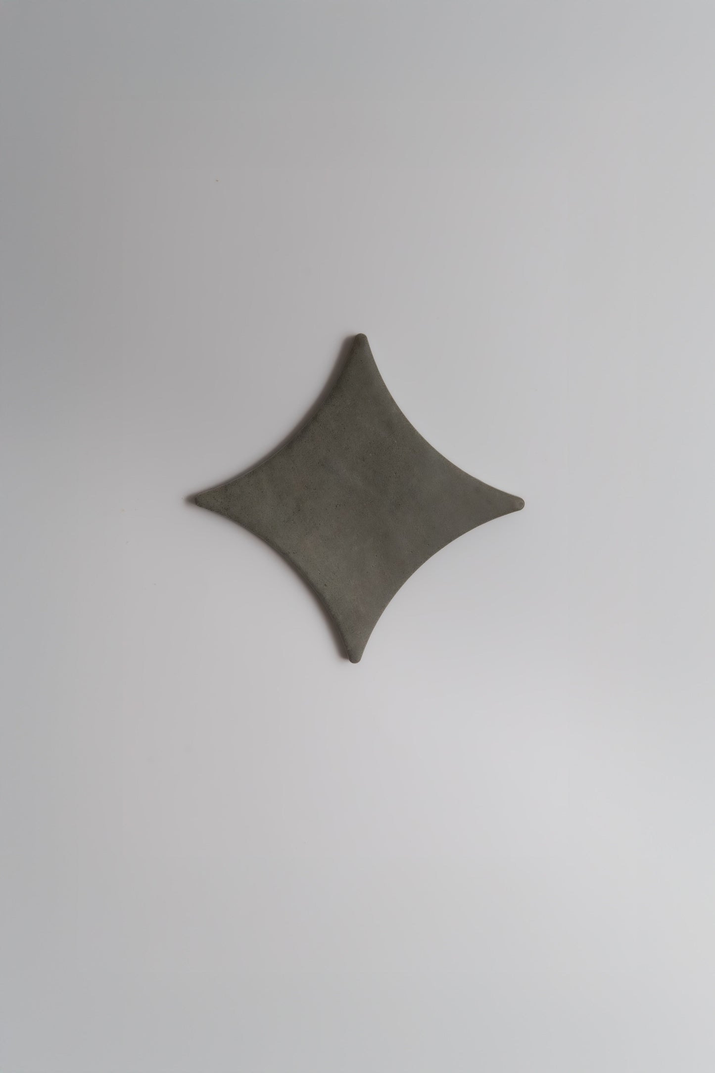 The Finca Cardon Sample is a dark gray, rhombus-shaped object with curved edges on a light gray background.