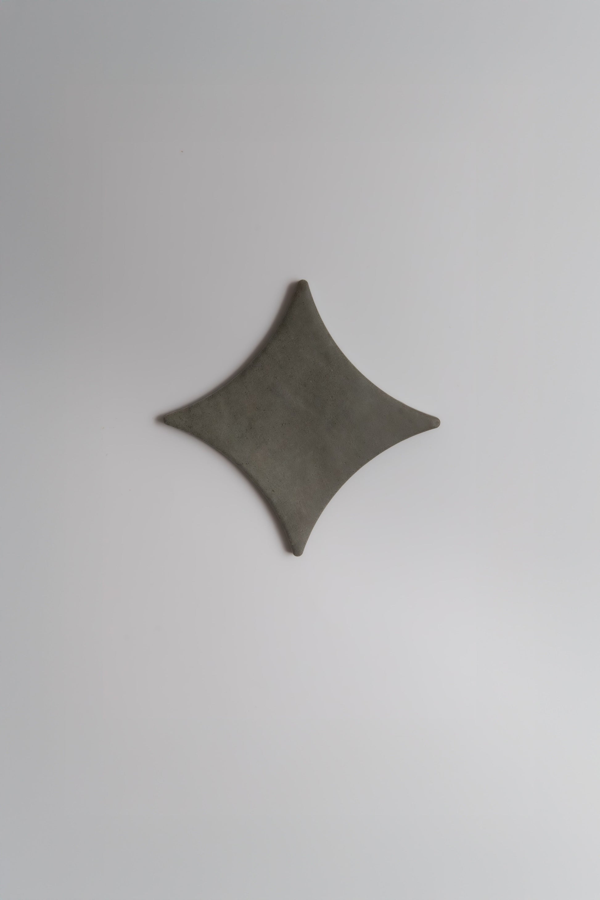 The Finca Cardon Sample is a dark gray, rhombus-shaped object with curved edges on a light gray background.
